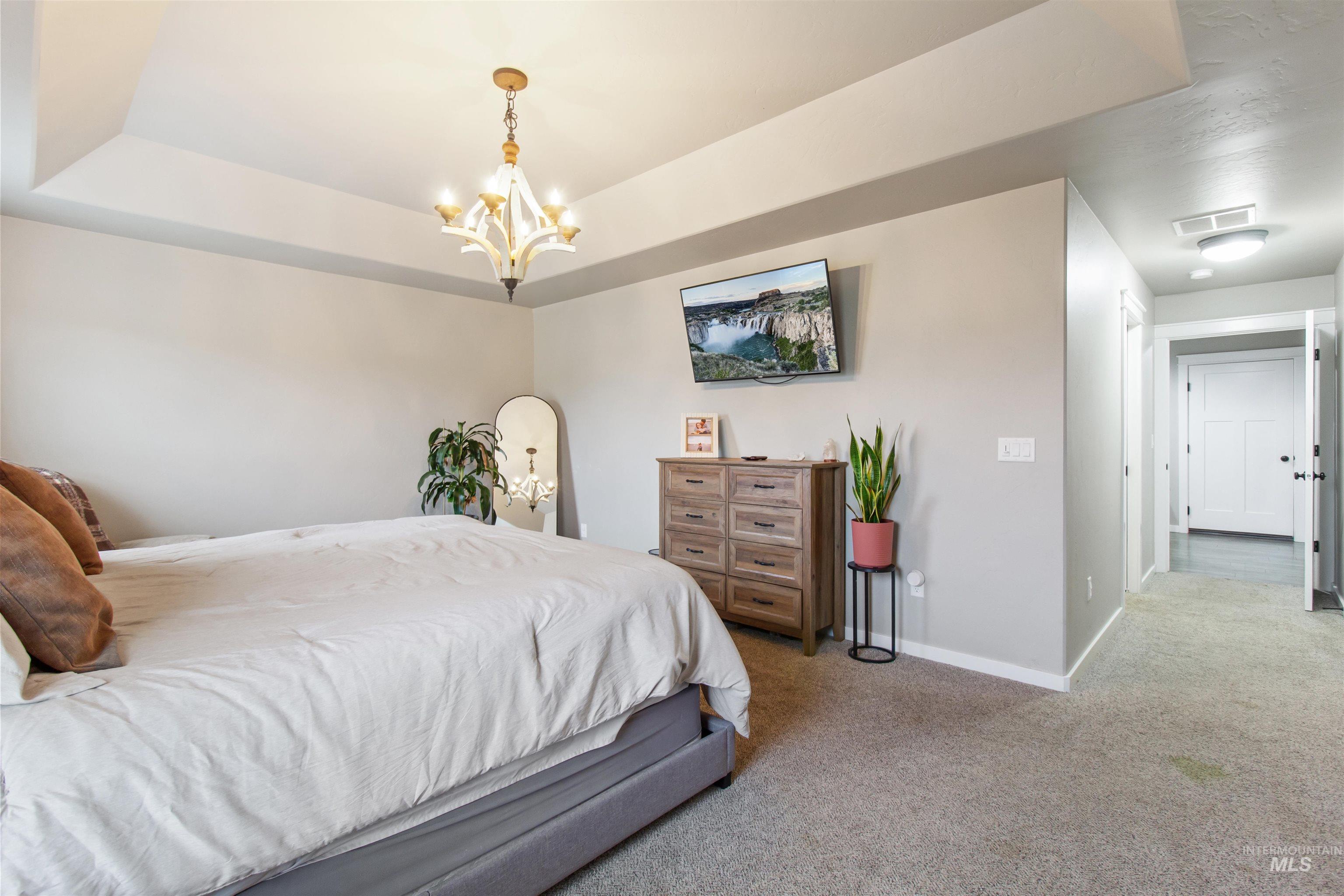 Bedroom with carpet floors, a tray ceiling, and a chandelier