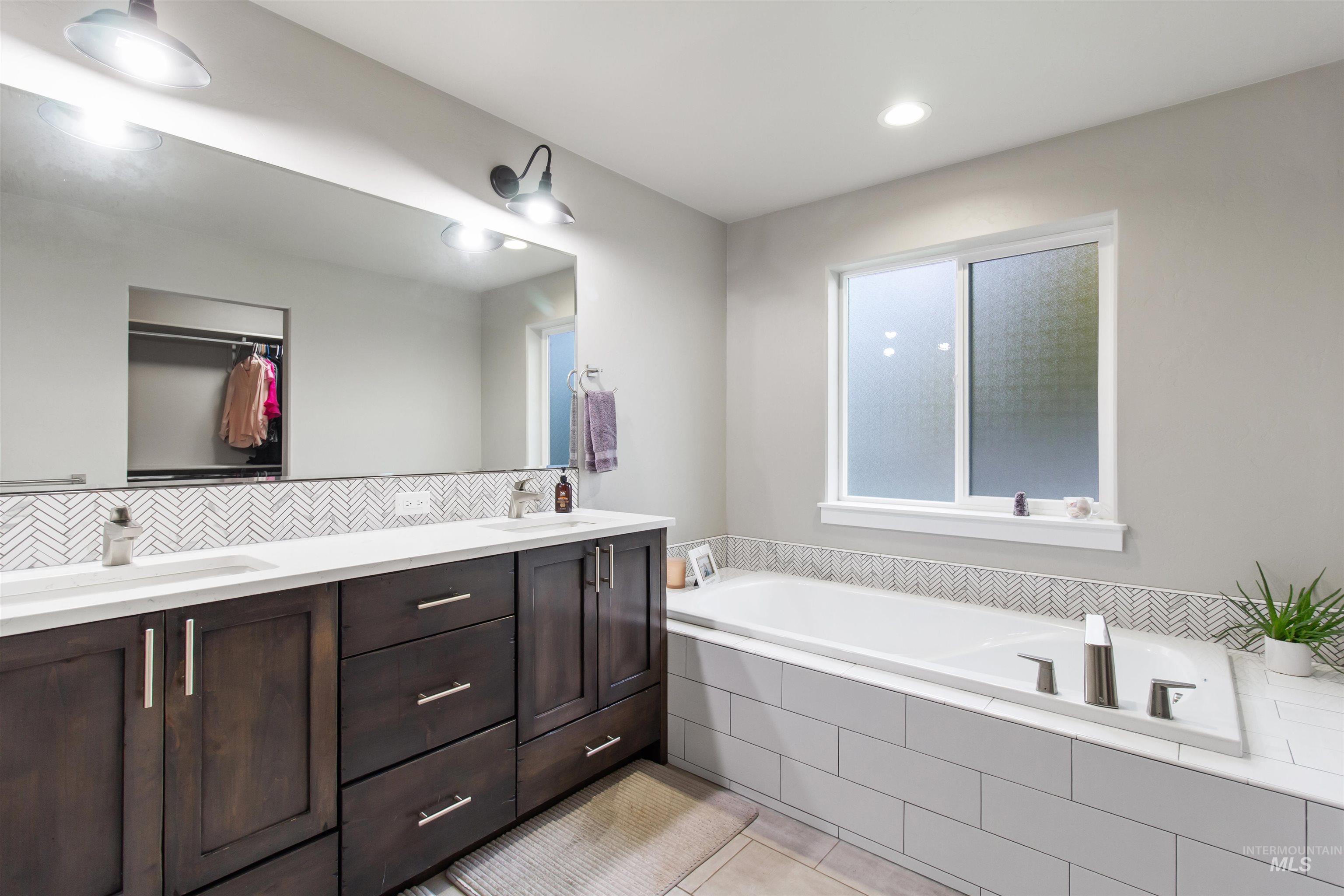 Bathroom featuring double vanity, a bath, a spacious closet, light tile patterned floors, and recessed lighting