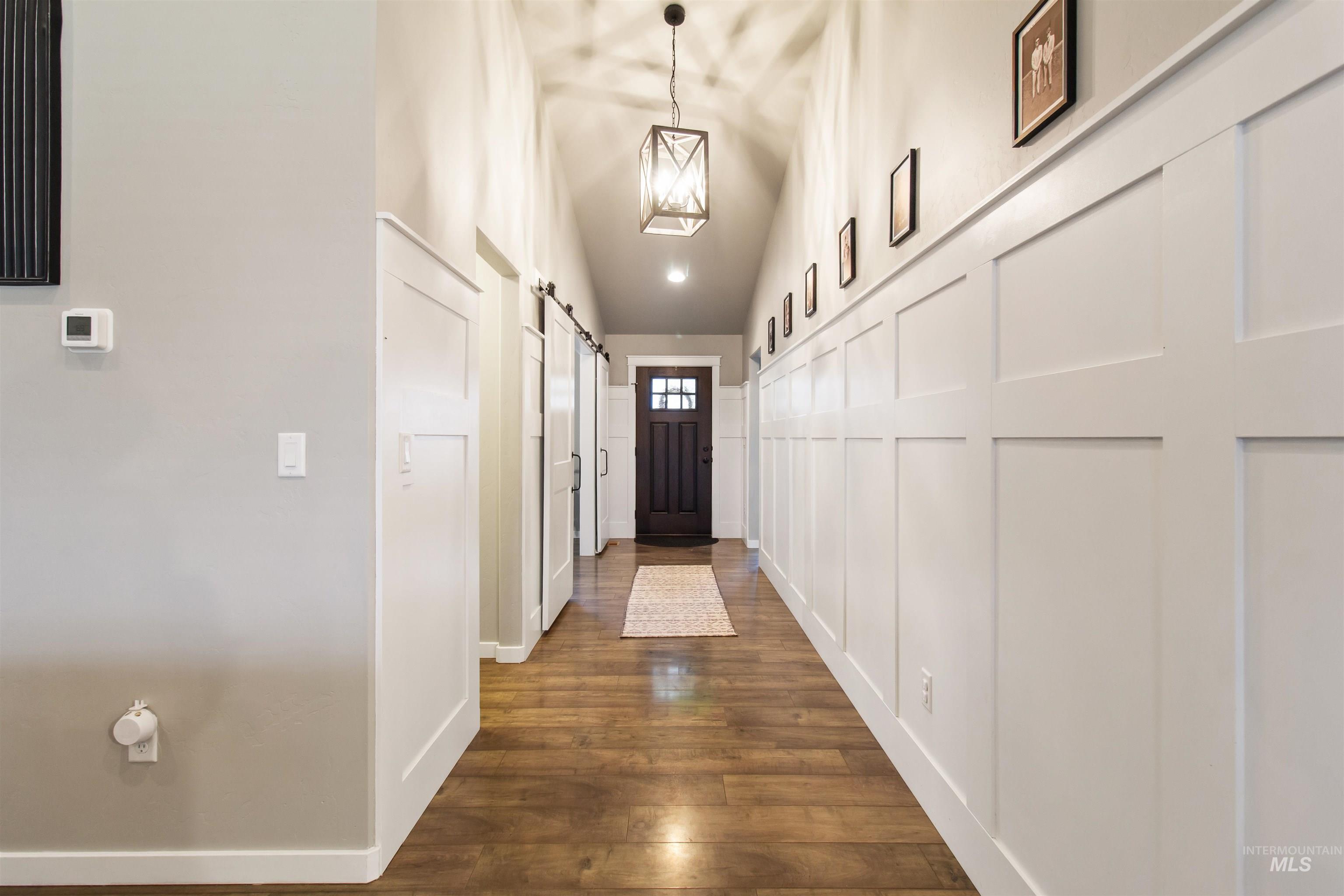 Corridor featuring vaulted ceiling, dark wood-style flooring, a barn door, and a decorative wall