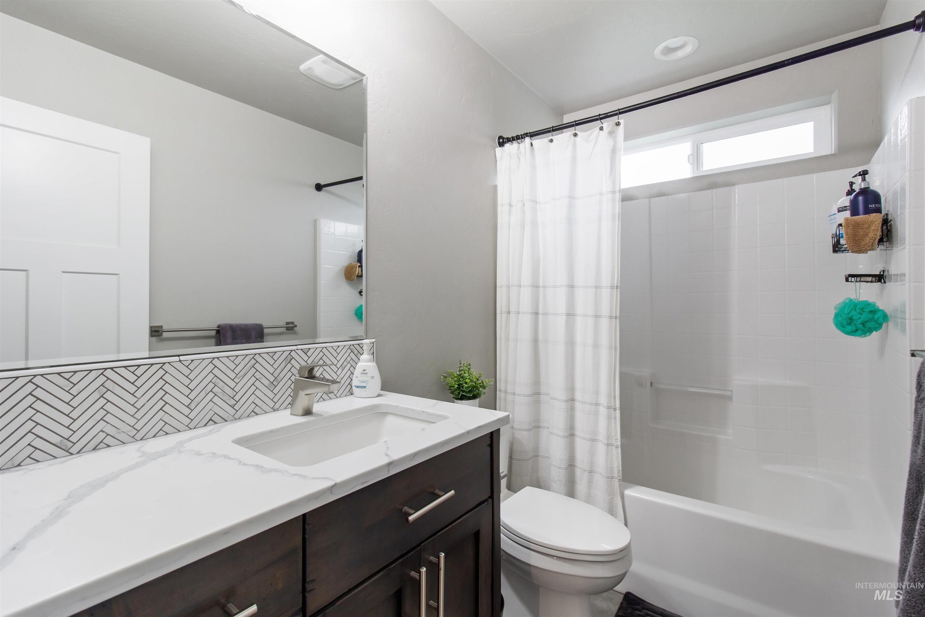 Full bath featuring vanity, shower / bath combo, and decorative backsplash