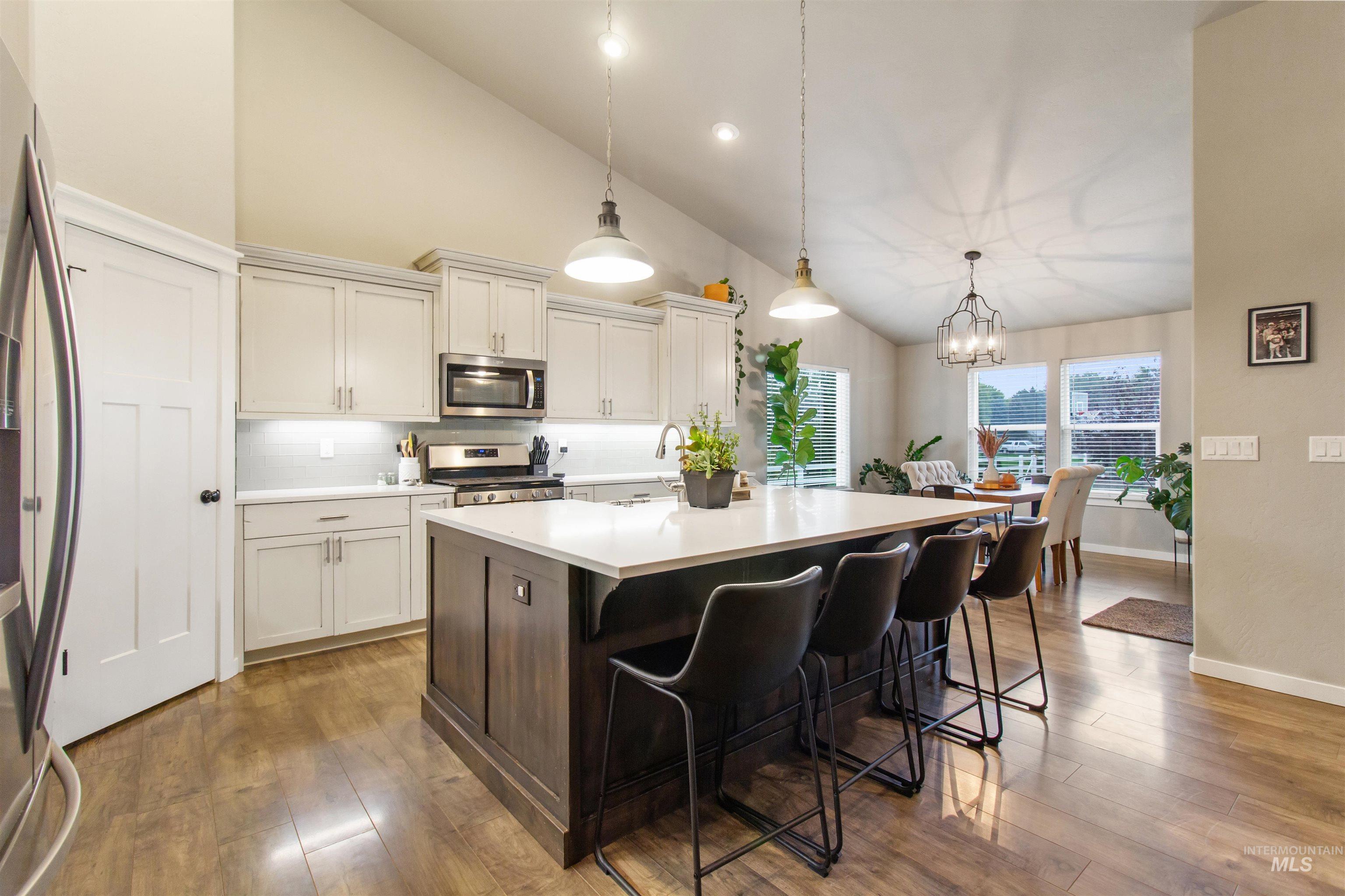 Kitchen featuring decorative backsplash, decorative light fixtures, a center island with sink, dark brown cabinets, and stainless steel appliances