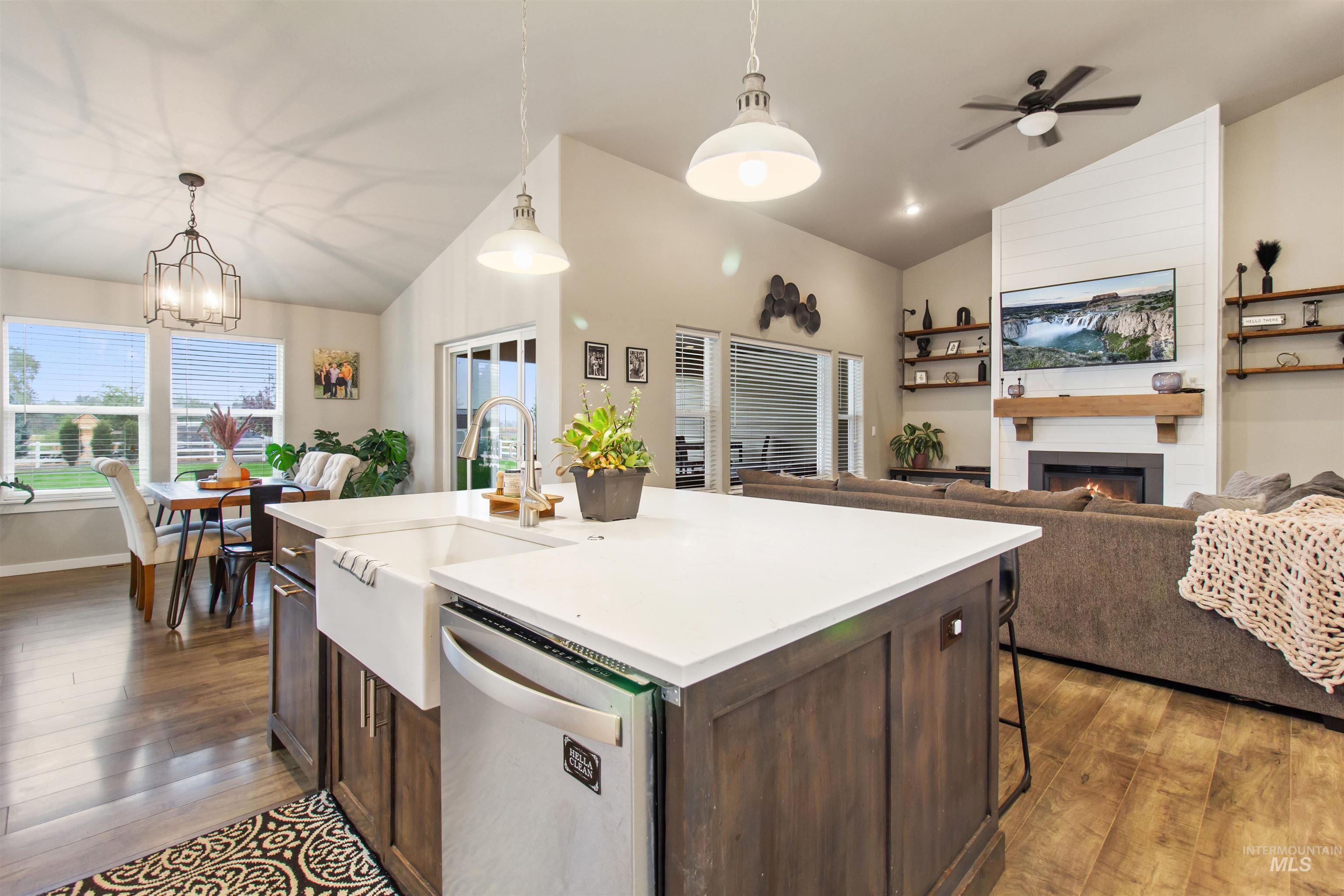 Kitchen with lofted ceiling, dark brown cabinets, hanging light fixtures, dishwasher, and a fireplace