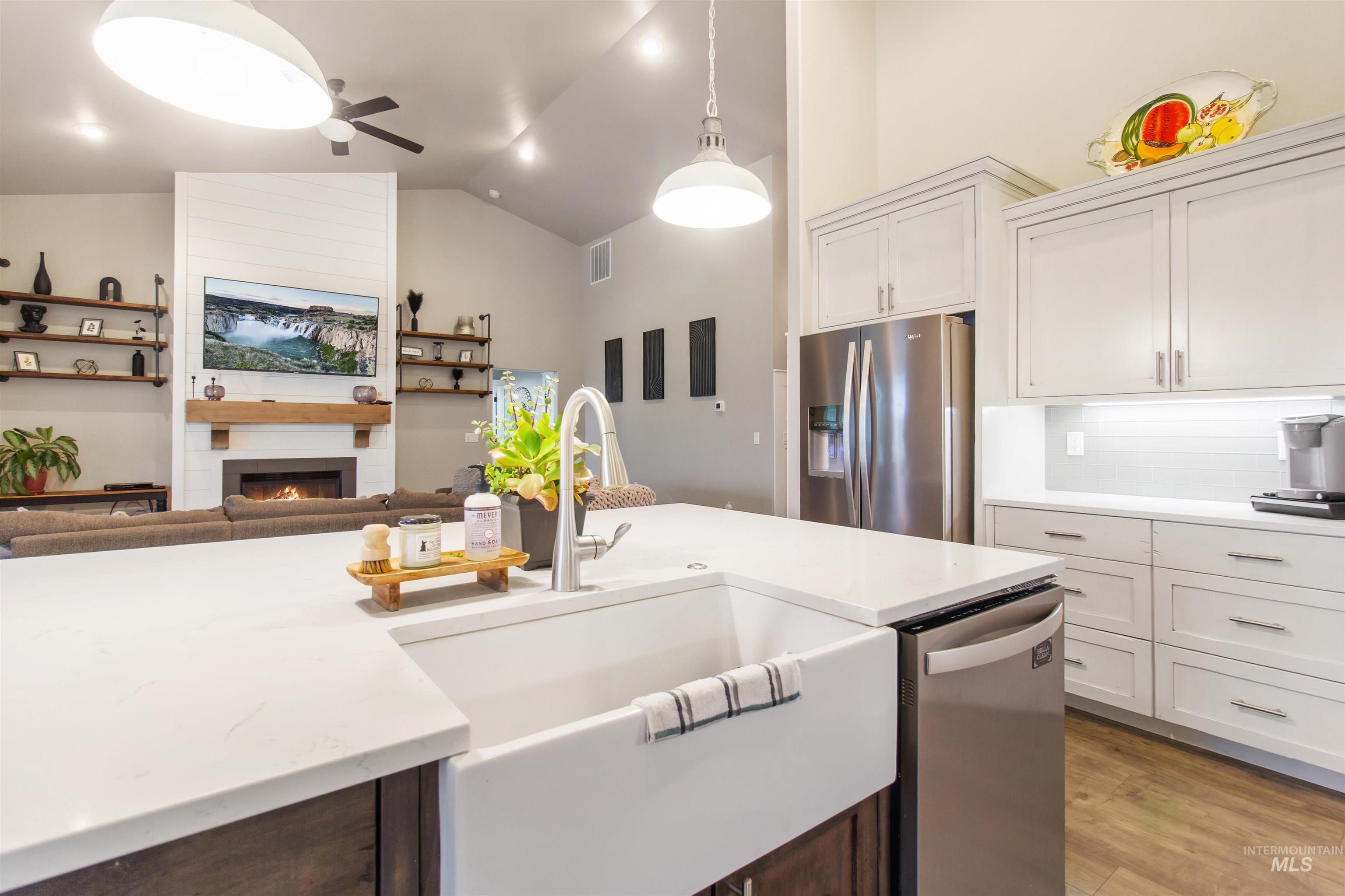 Kitchen featuring open floor plan, stainless steel appliances, a fireplace, light wood-style floors, and white cabinets