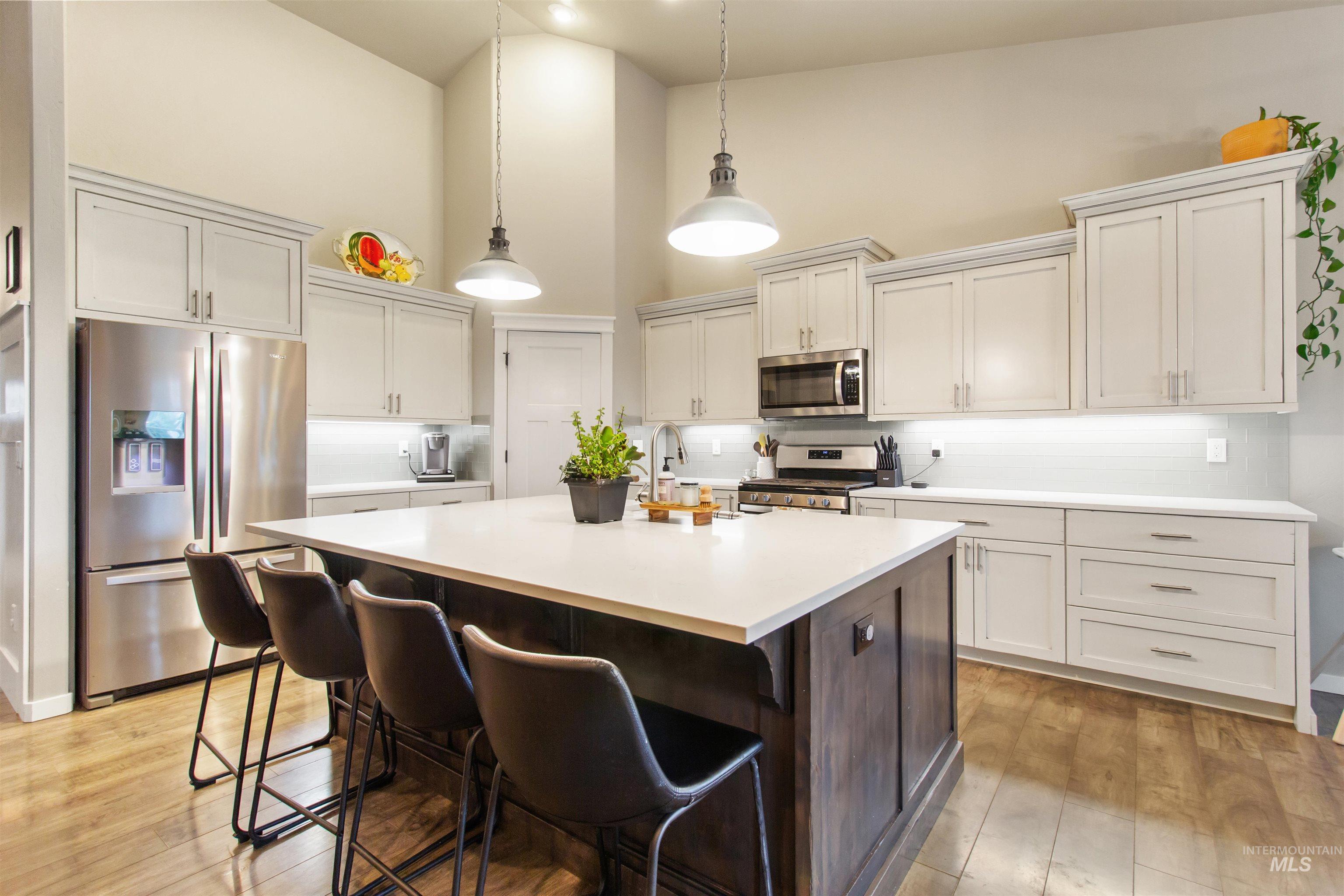 Kitchen with appliances with stainless steel finishes, tasteful backsplash, dark brown cabinets, an island with sink, and decorative light fixtures