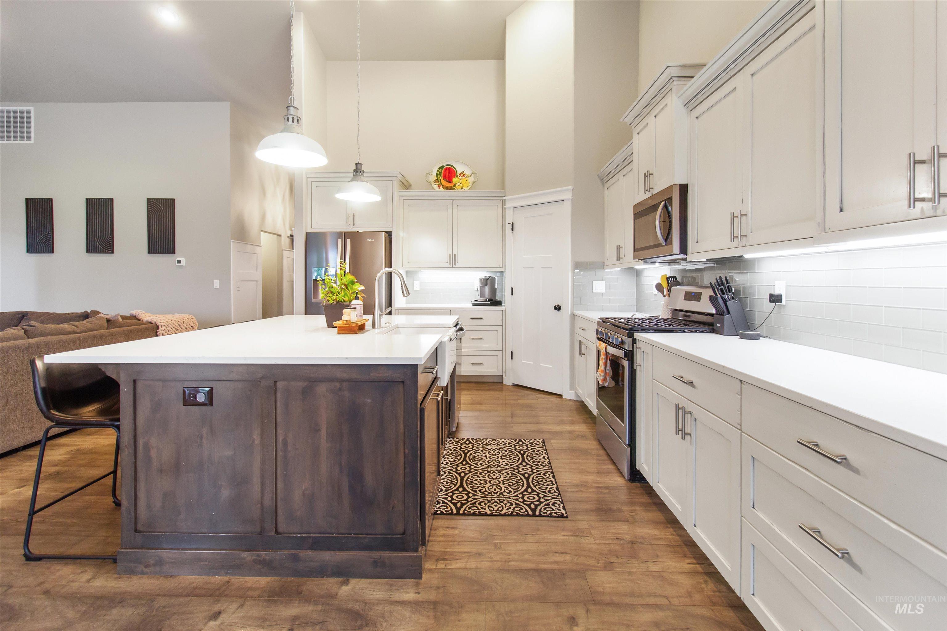 Kitchen featuring open floor plan, appliances with stainless steel finishes, a high ceiling, decorative light fixtures, and backsplash