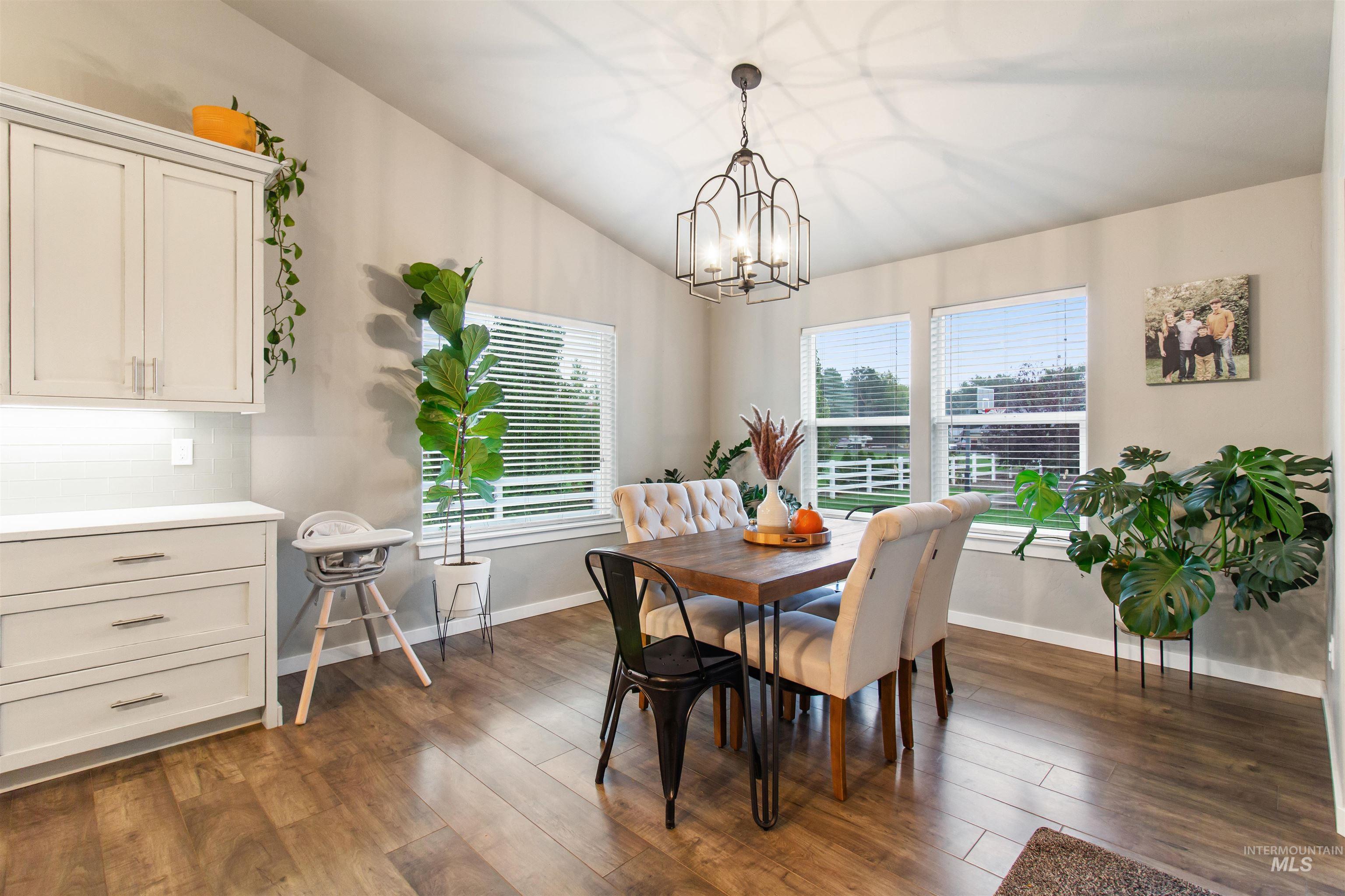 Dining space with dark wood-style flooring, vaulted ceiling, and a chandelier