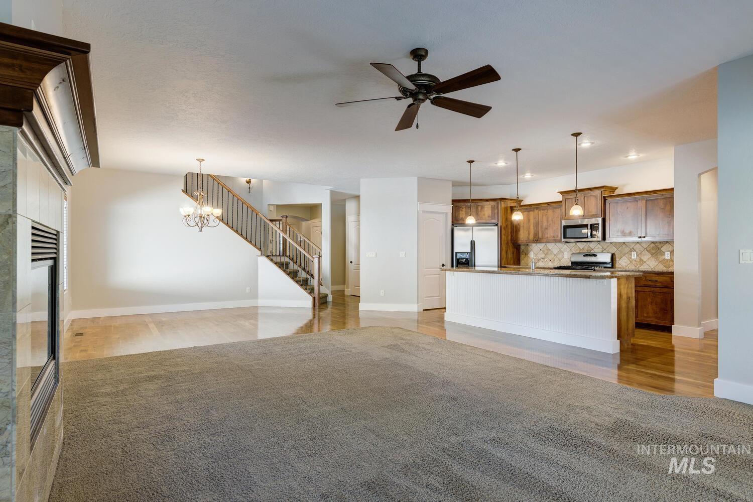 Unfurnished living room with a chandelier, ceiling fan, light wood-style flooring, stairway, and a fireplace