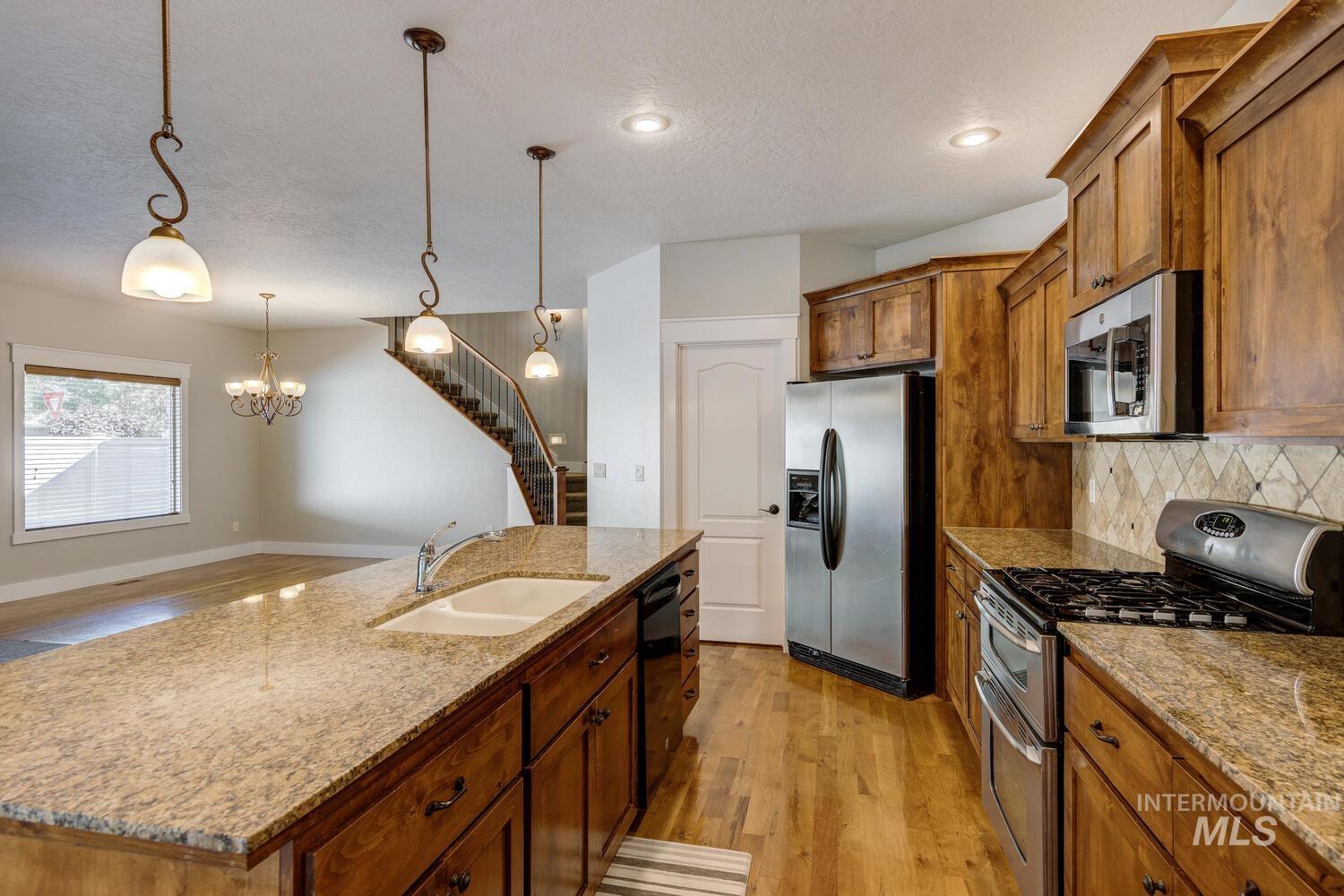 Kitchen with light wood-style flooring, appliances with stainless steel finishes, brown cabinets, a center island with sink, and pendant lighting