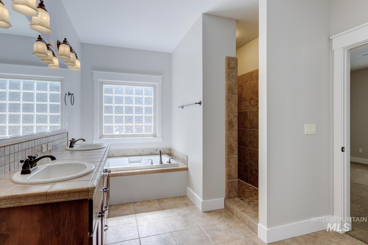 Full bathroom with tiled shower, a bath, light tile patterned floors, and double vanity