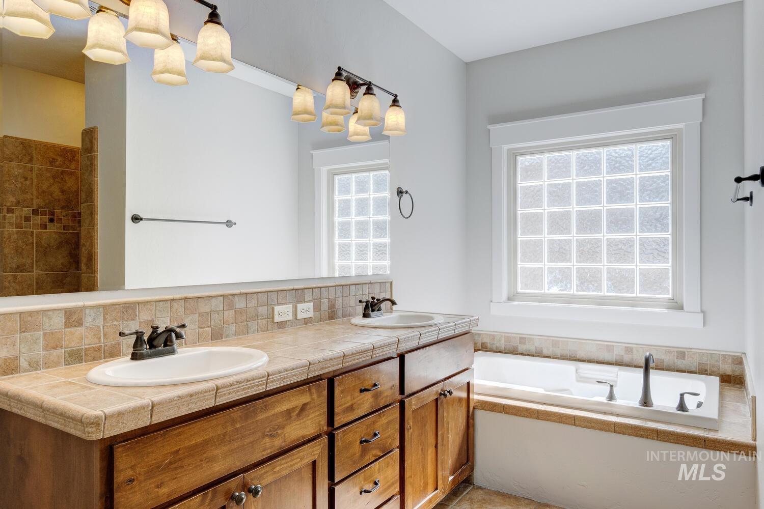 Bathroom featuring plenty of natural light, a bath, double vanity, and tasteful backsplash