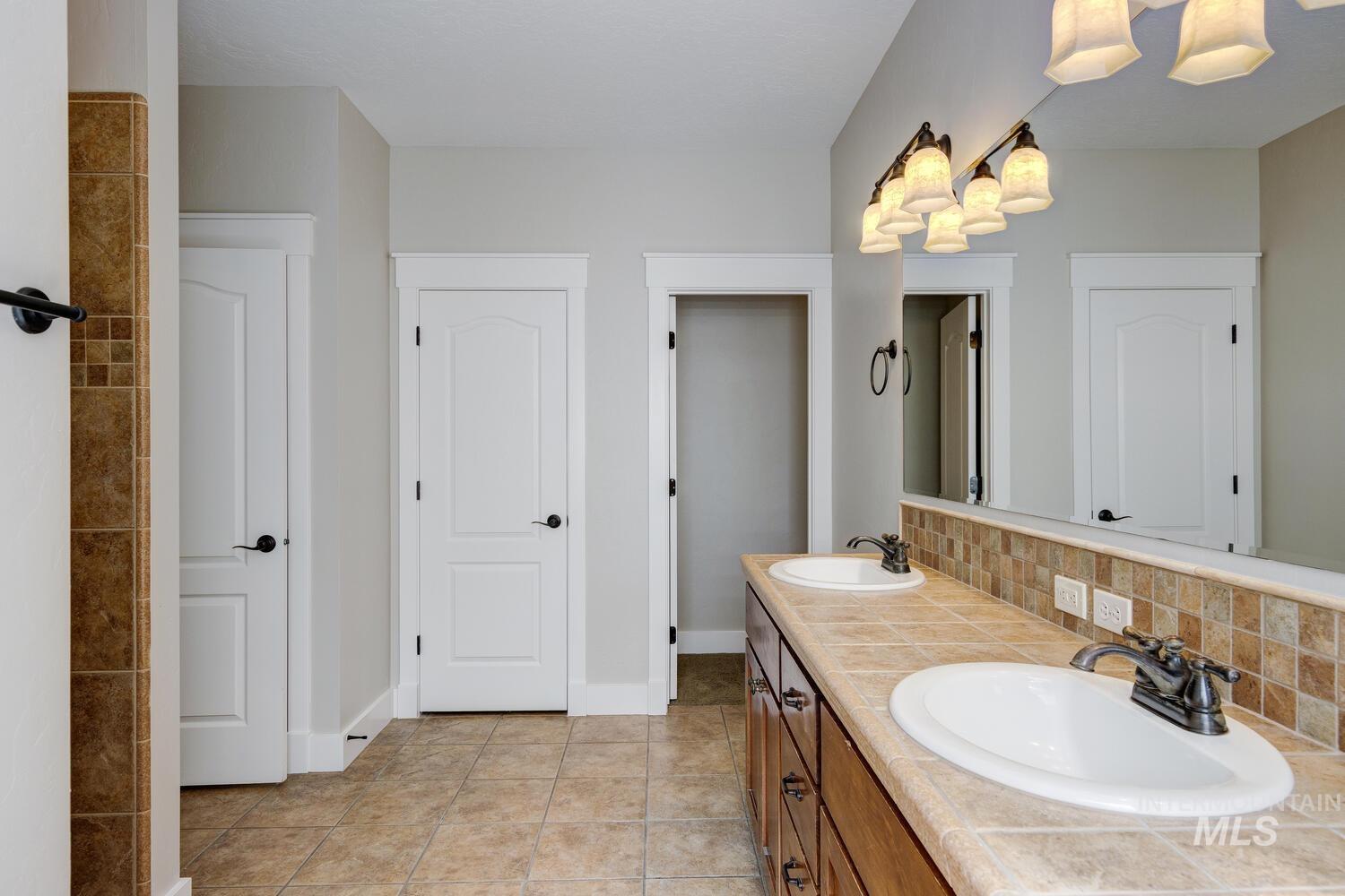 Bathroom featuring double vanity, backsplash, and light tile patterned flooring