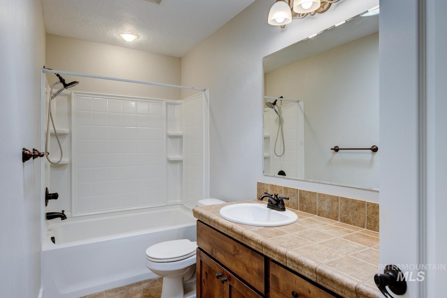 Full bath featuring shower / tub combination, vanity, a textured ceiling, and light tile patterned floors
