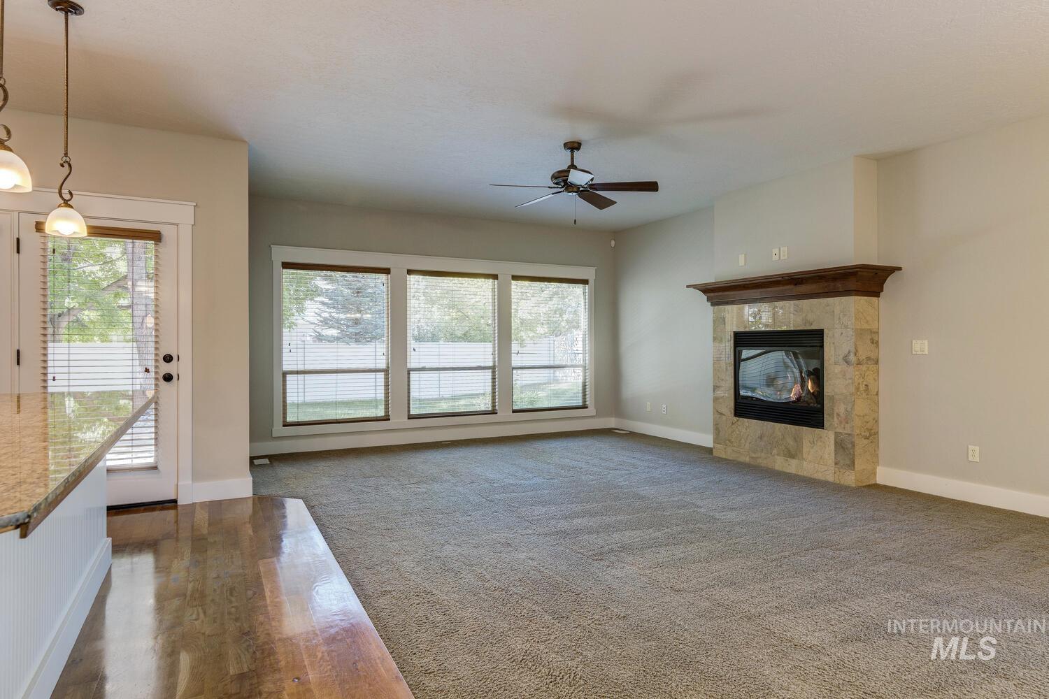 Unfurnished living room featuring a fireplace, ceiling fan, and dark colored carpet