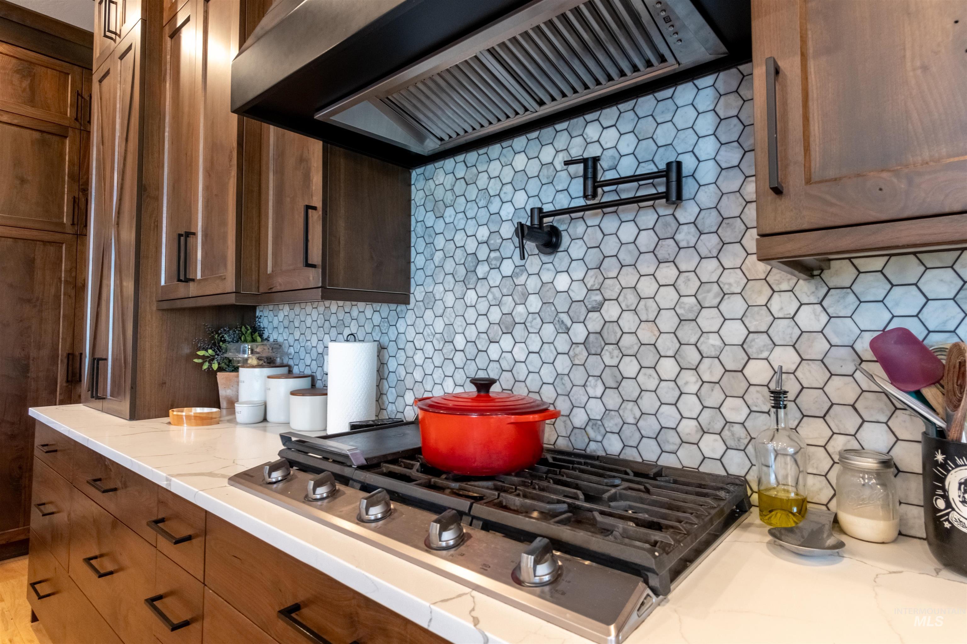 Kitchen featuring custom exhaust hood, stainless steel gas stovetop, tasteful backsplash, and light stone counters