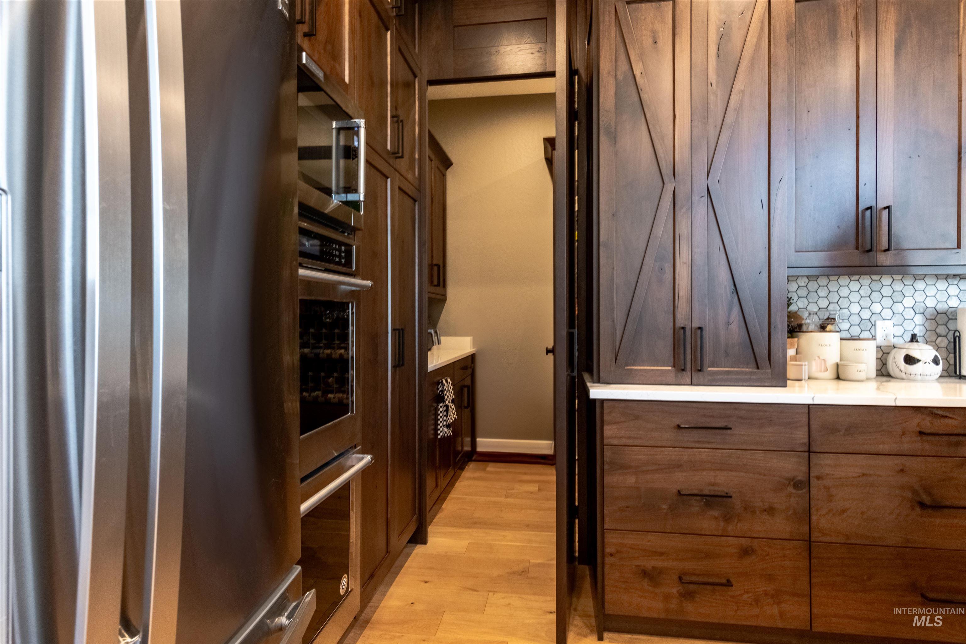 Kitchen with stainless steel appliances, light wood-style floors, backsplash, and light countertops