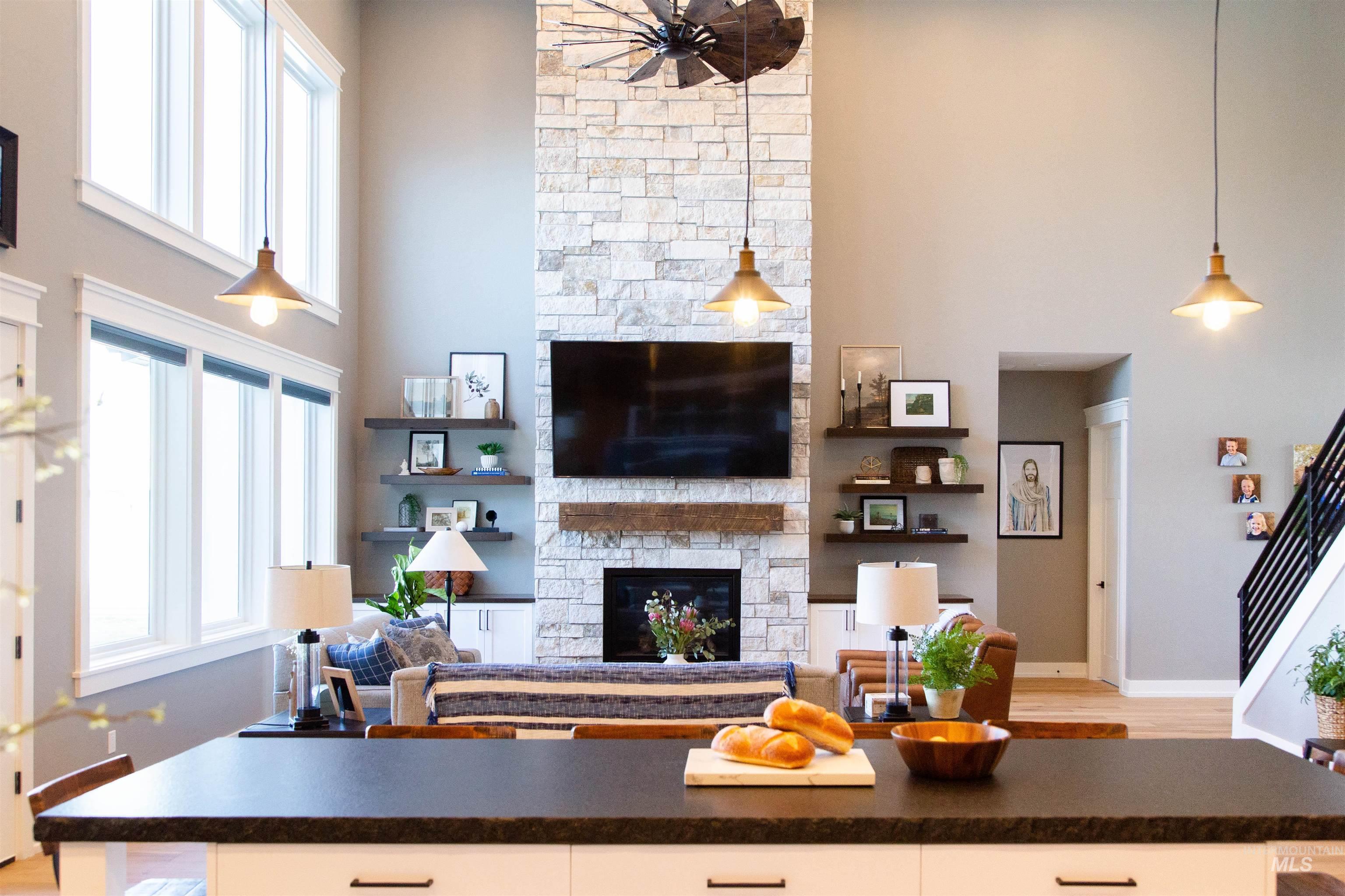 Living room with a high ceiling, a stone fireplace, a ceiling fan, and light wood finished floors