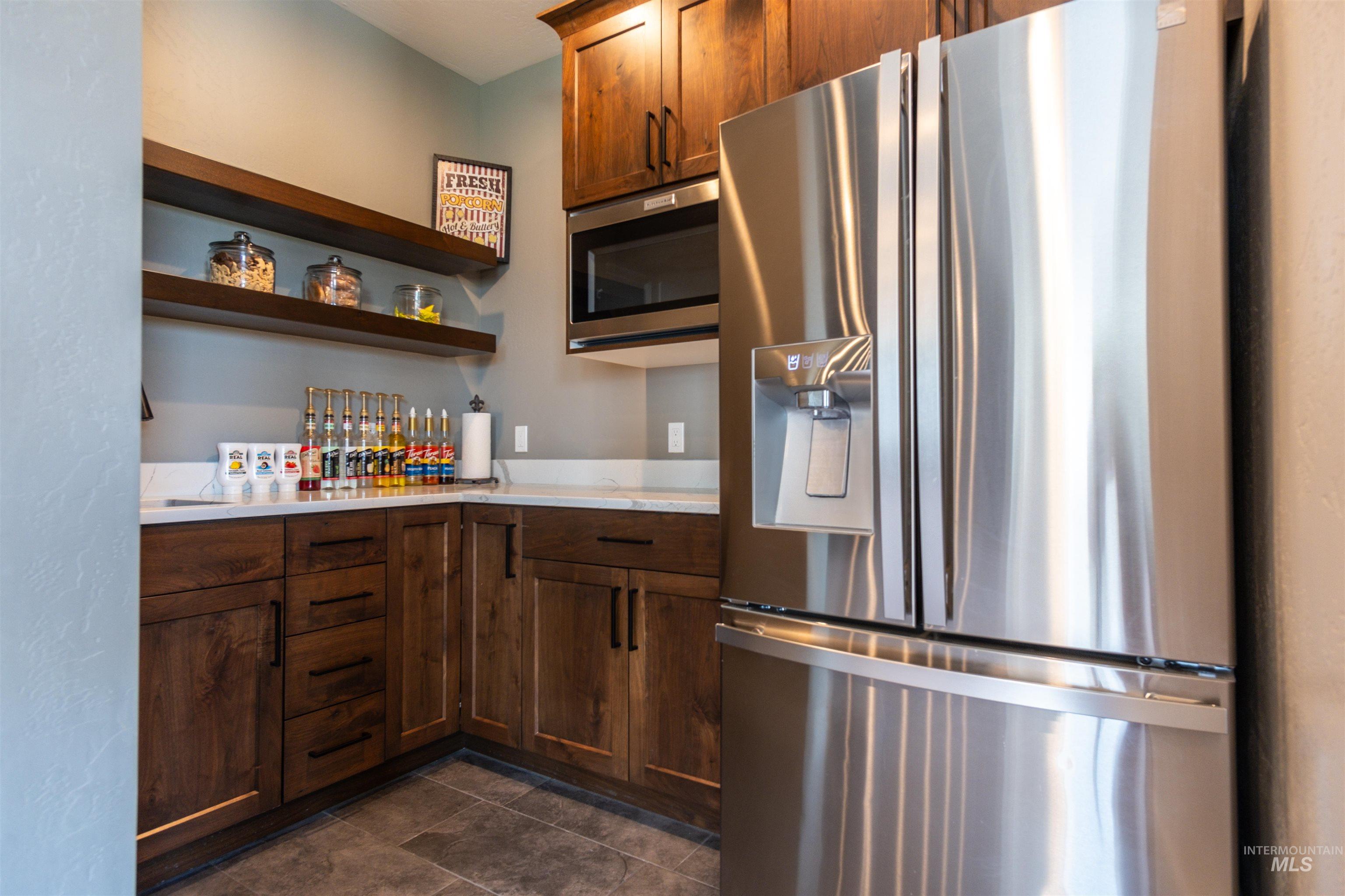 Kitchen with stainless steel appliances, open shelves, light countertops, and dark tile patterned flooring