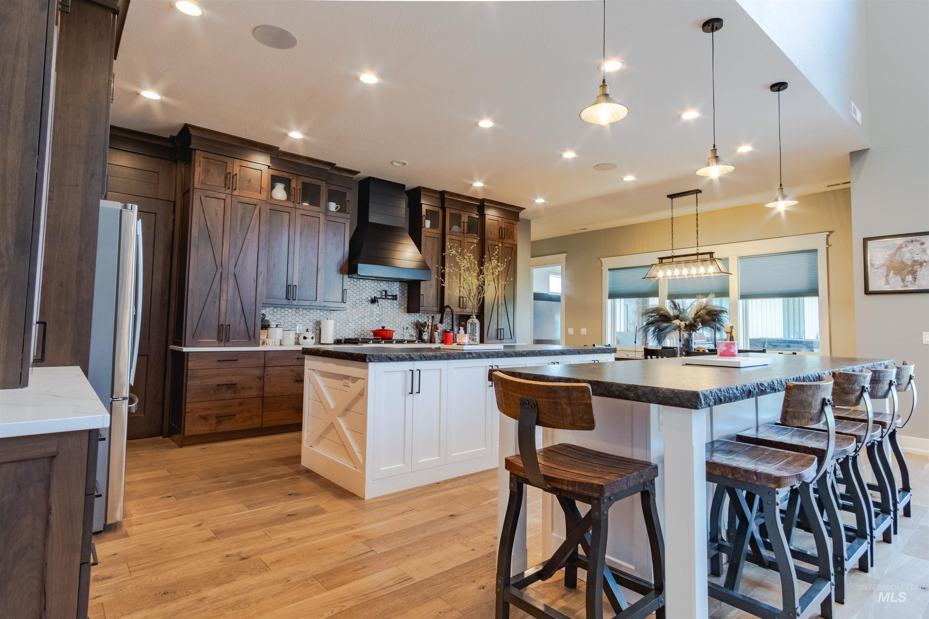 Kitchen featuring a large island, light wood-style floors, decorative backsplash, custom range hood, and glass insert cabinets