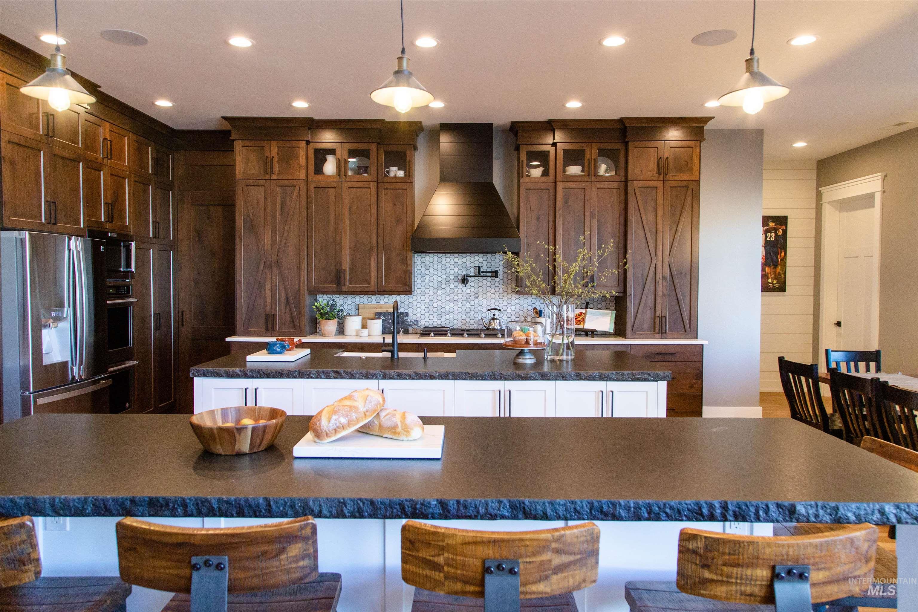 Kitchen featuring a kitchen island with sink, stainless steel fridge, tasteful backsplash, wall chimney exhaust hood, and glass insert cabinets