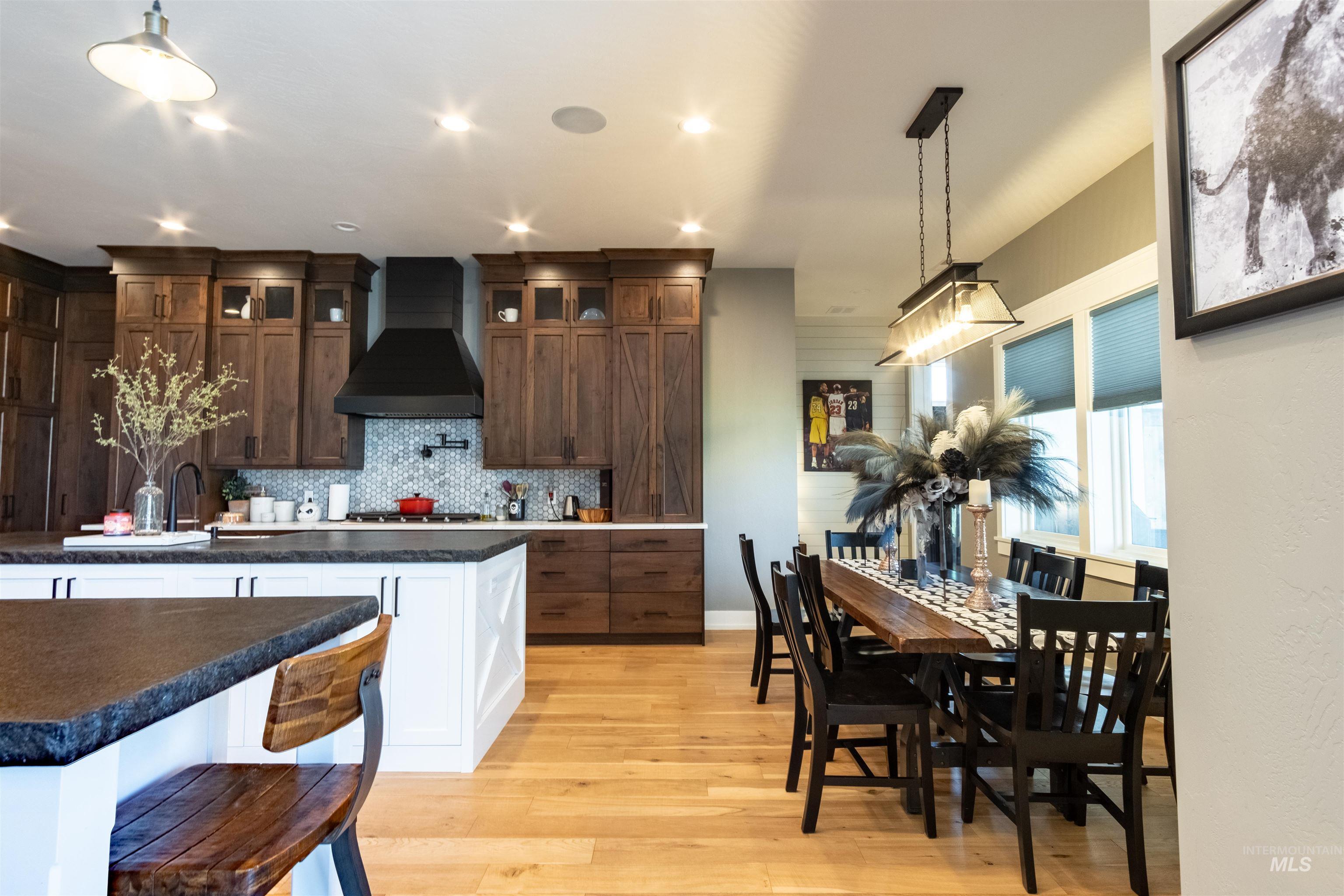 Kitchen featuring light wood finished floors, wall chimney range hood, tasteful backsplash, glass insert cabinets, and dark countertops