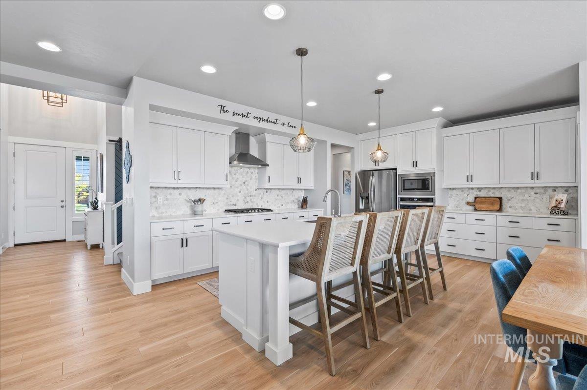 Kitchen with stainless steel appliances, wall chimney exhaust hood, backsplash, light countertops, and recessed lighting