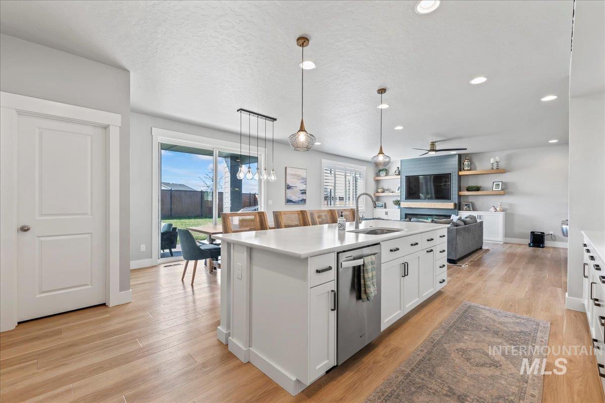 Kitchen featuring white cabinets, light wood finished floors, a kitchen island with sink, a textured ceiling, and dishwasher