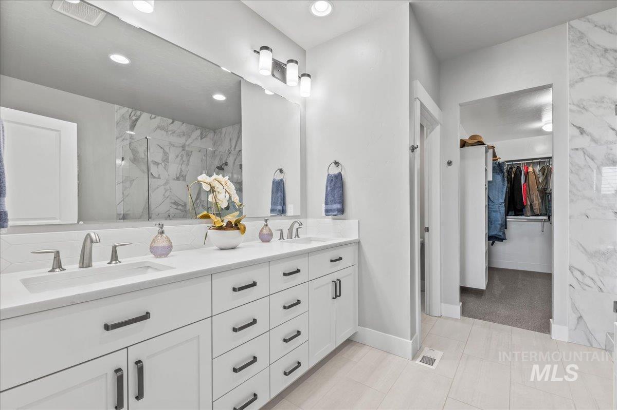 Bathroom with a marble finish shower, double vanity, a walk in closet, and recessed lighting