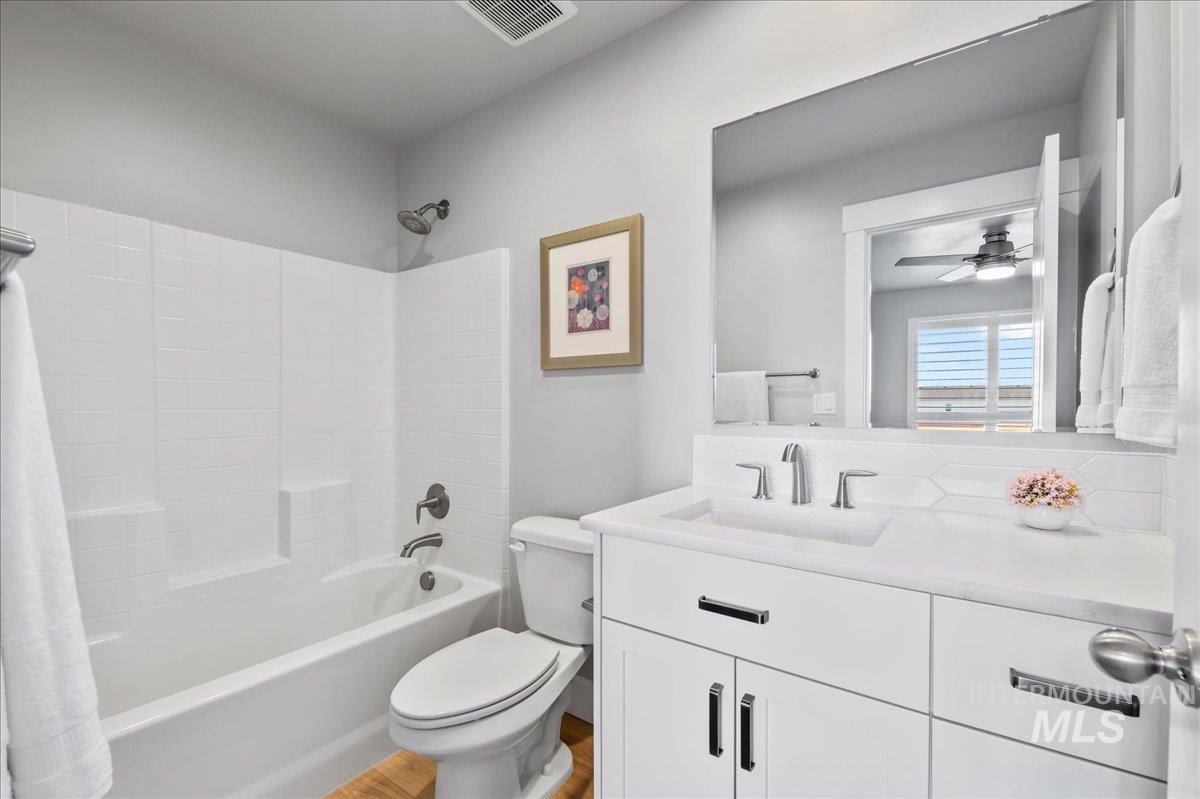Bathroom ensuite, featuring vanity, tub / shower combination, a ceiling fan, and wood finished floors