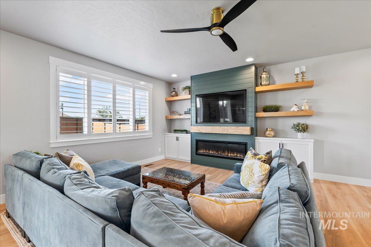 Living room featuring ceiling fan, a large fireplace, light wood-style flooring, and recessed lighting