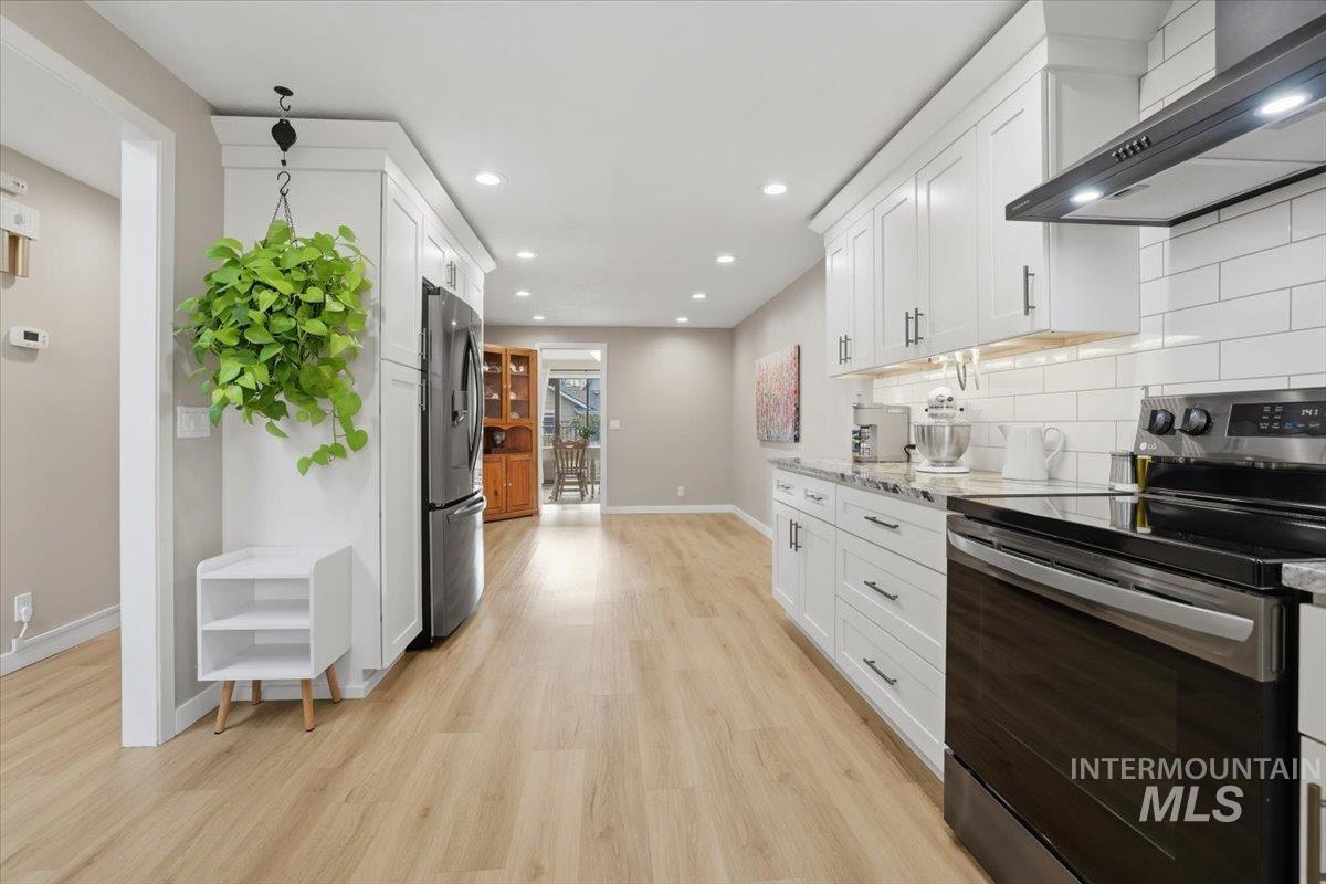 Kitchen featuring stainless steel appliances, white cabinetry, wall chimney range hood, light stone counters, and recessed lighting