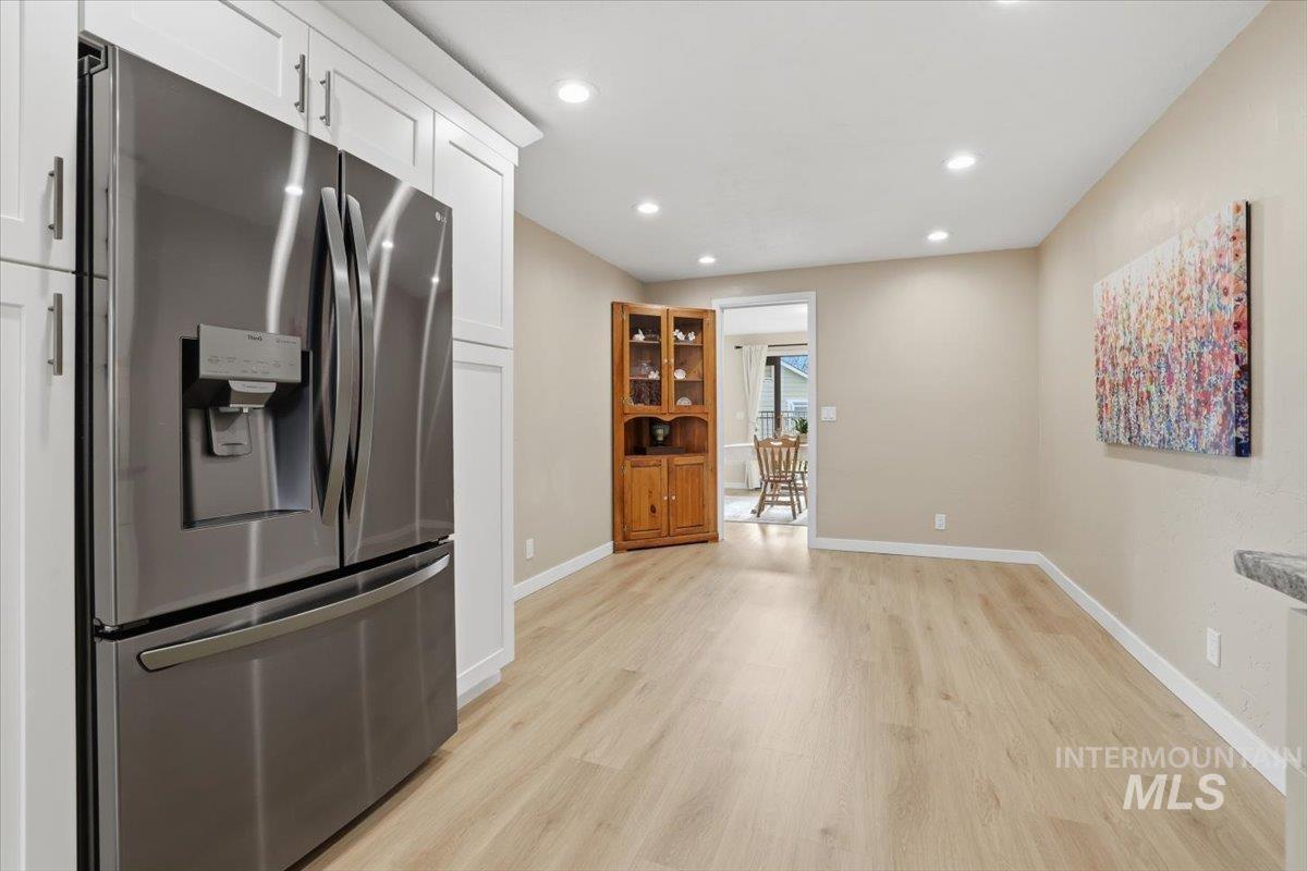 Kitchen featuring stainless steel fridge with ice dispenser, light wood-style flooring, recessed lighting, and white cabinetry
