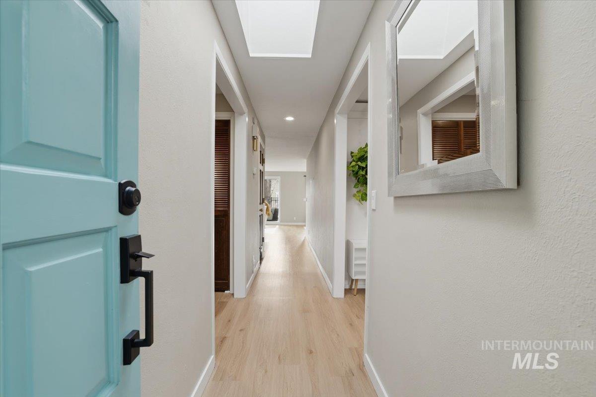 Hallway featuring light wood-type flooring, a skylight, recessed lighting, and a textured wall