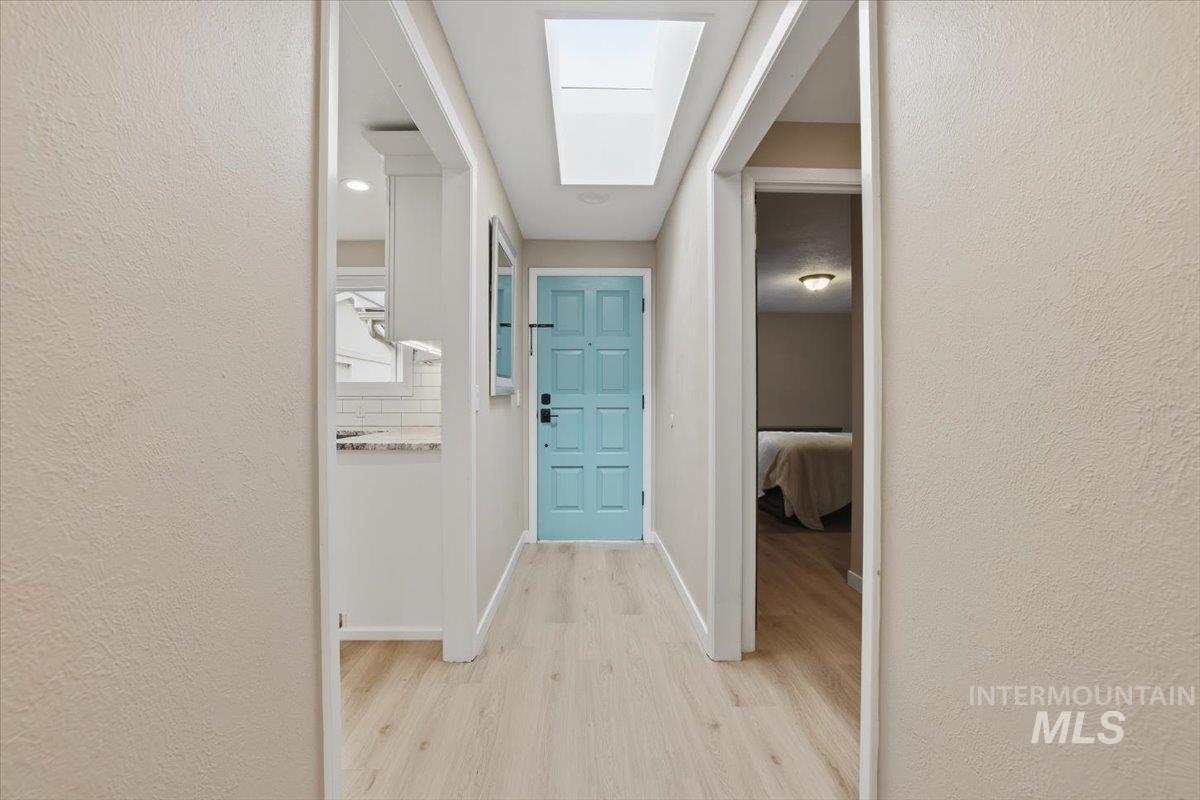 Hallway with a textured wall, light wood finished floors, and a skylight
