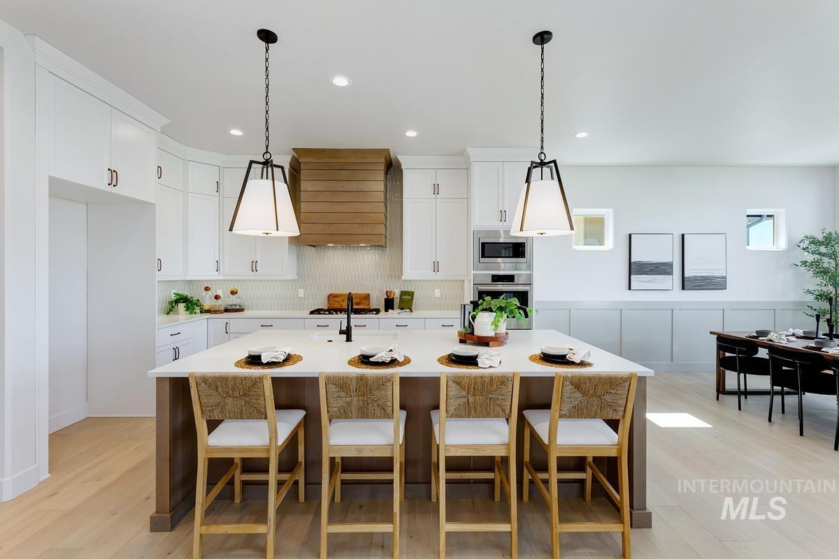 Kitchen with pendant lighting, white cabinets, a breakfast bar, custom exhaust hood, and appliances with stainless steel finishes