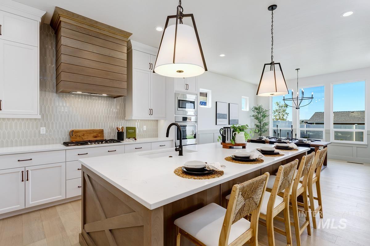 Kitchen with white cabinets, a center island with sink, light wood-type flooring, tasteful backsplash, and decorative light fixtures