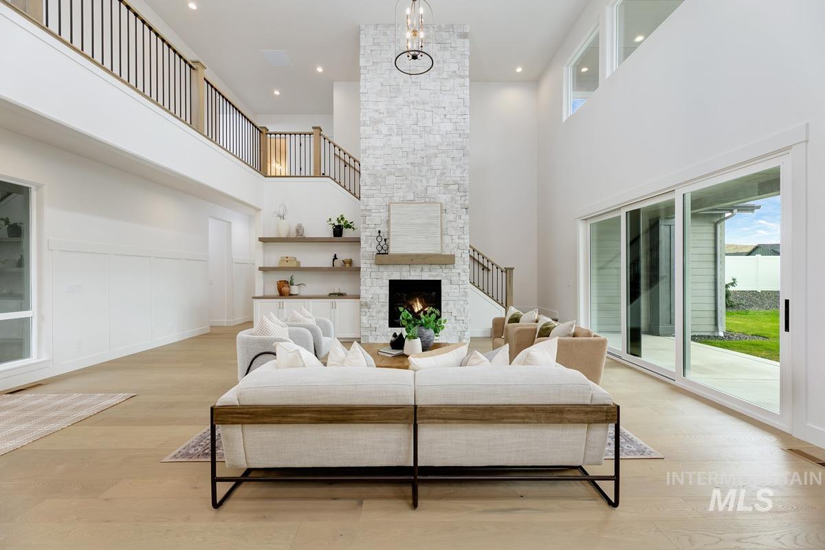 Living area with a towering ceiling, light wood-type flooring, a stone fireplace, recessed lighting, and a decorative wall