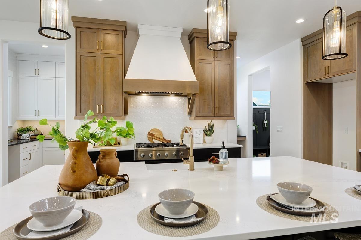 Kitchen featuring hanging light fixtures, custom exhaust hood, light stone counters, and recessed lighting