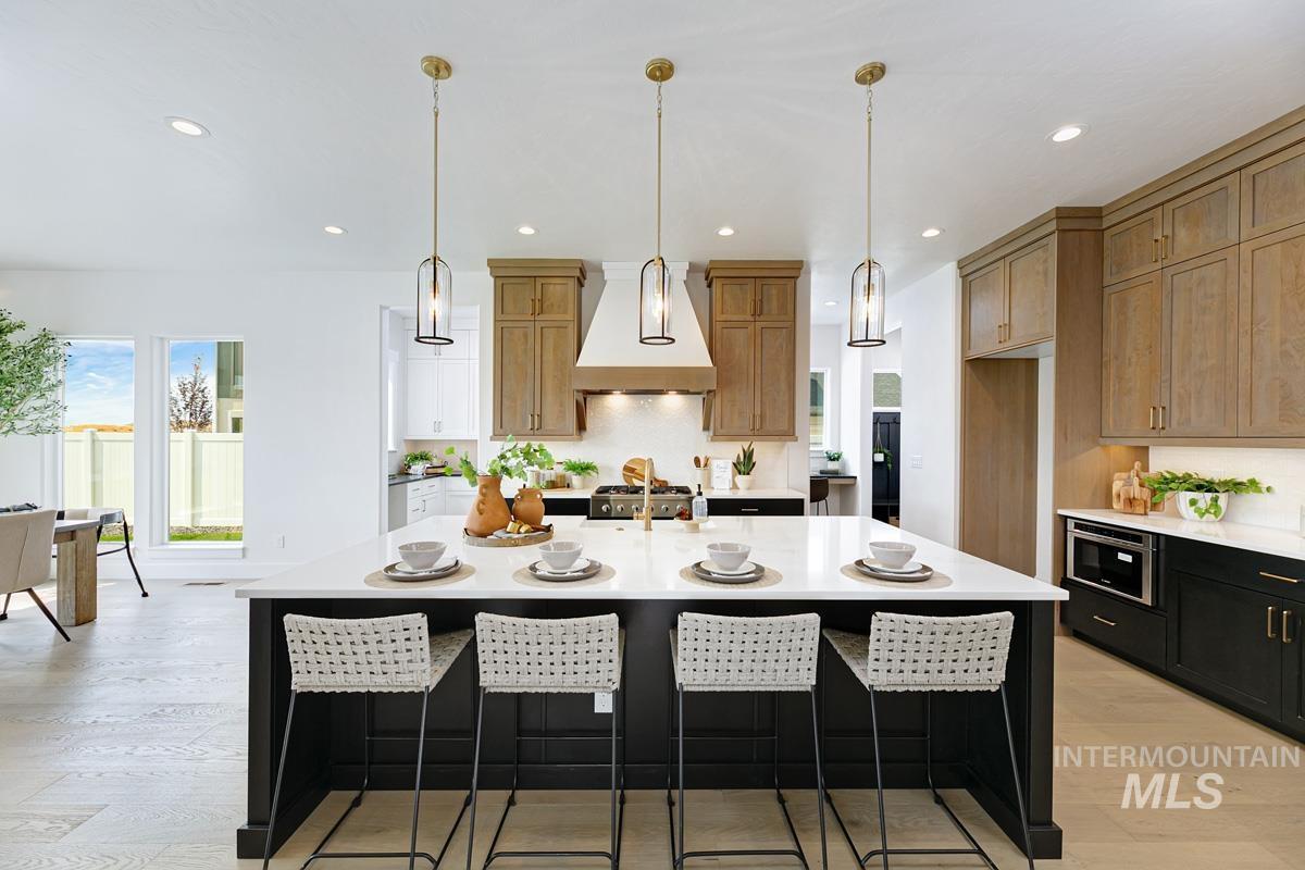 Kitchen featuring a kitchen bar, pendant lighting, custom range hood, light stone countertops, and recessed lighting
