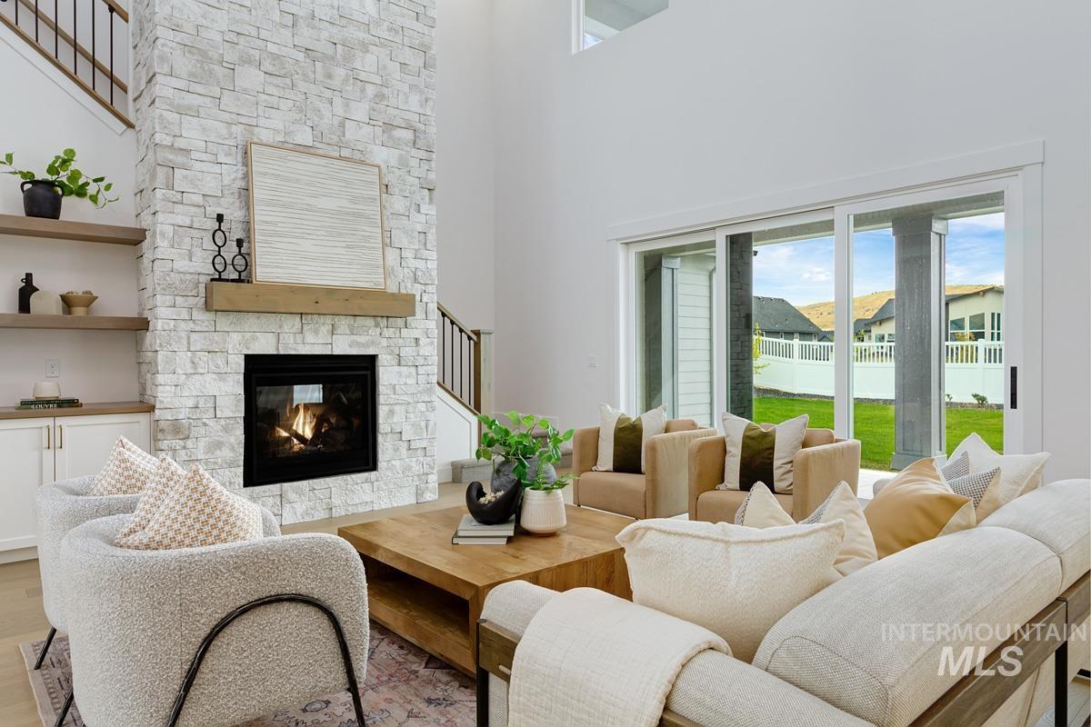 Living room featuring a stone fireplace, healthy amount of natural light, a towering ceiling, stairway, and wood finished floors