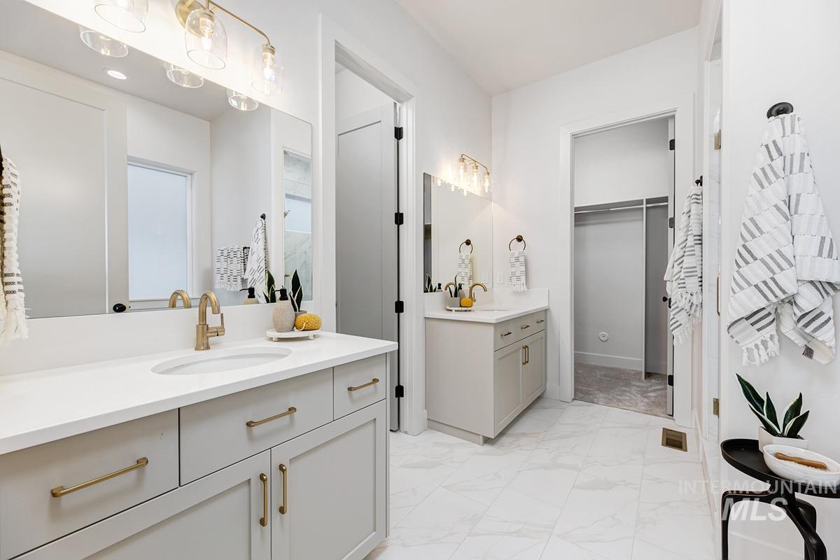 Full bathroom featuring two vanities, light marble finish flooring, and a walk in closet