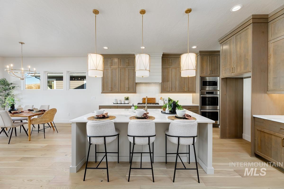 Kitchen featuring brown cabinetry, a breakfast bar, decorative light fixtures, an island with sink, and light stone countertops