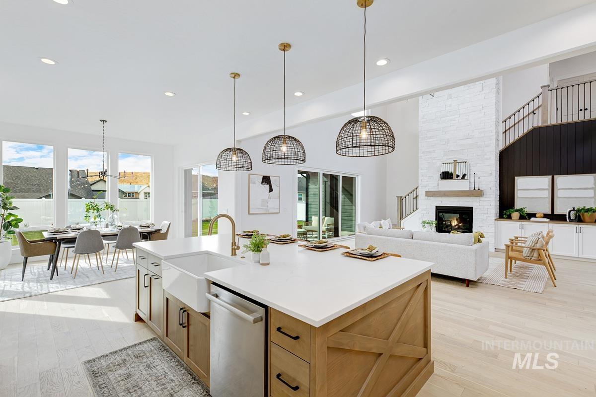 Kitchen with light wood-style floors, stainless steel dishwasher, a glass covered fireplace, hanging light fixtures, and open floor plan