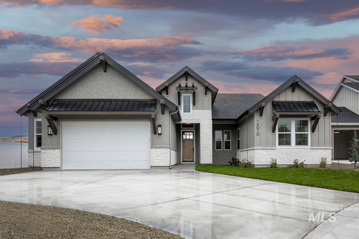 View of front facade with concrete driveway, a garage, board and batten siding, a metal roof, and a lawn