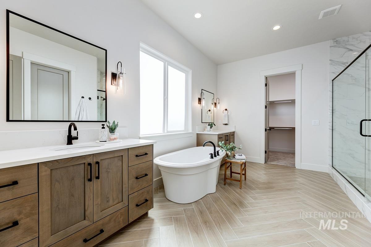 Bathroom featuring vanity, a walk in closet, a soaking tub, a marble finish shower, and recessed lighting
