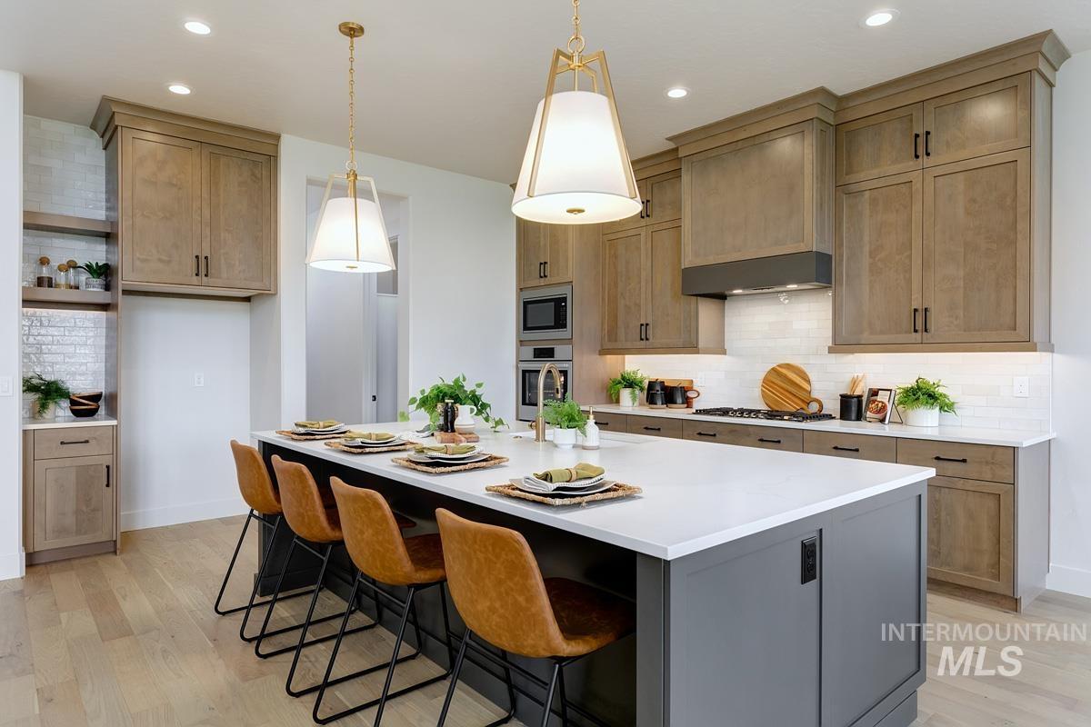 Kitchen with decorative backsplash, a kitchen bar, an island with sink, decorative light fixtures, and recessed lighting