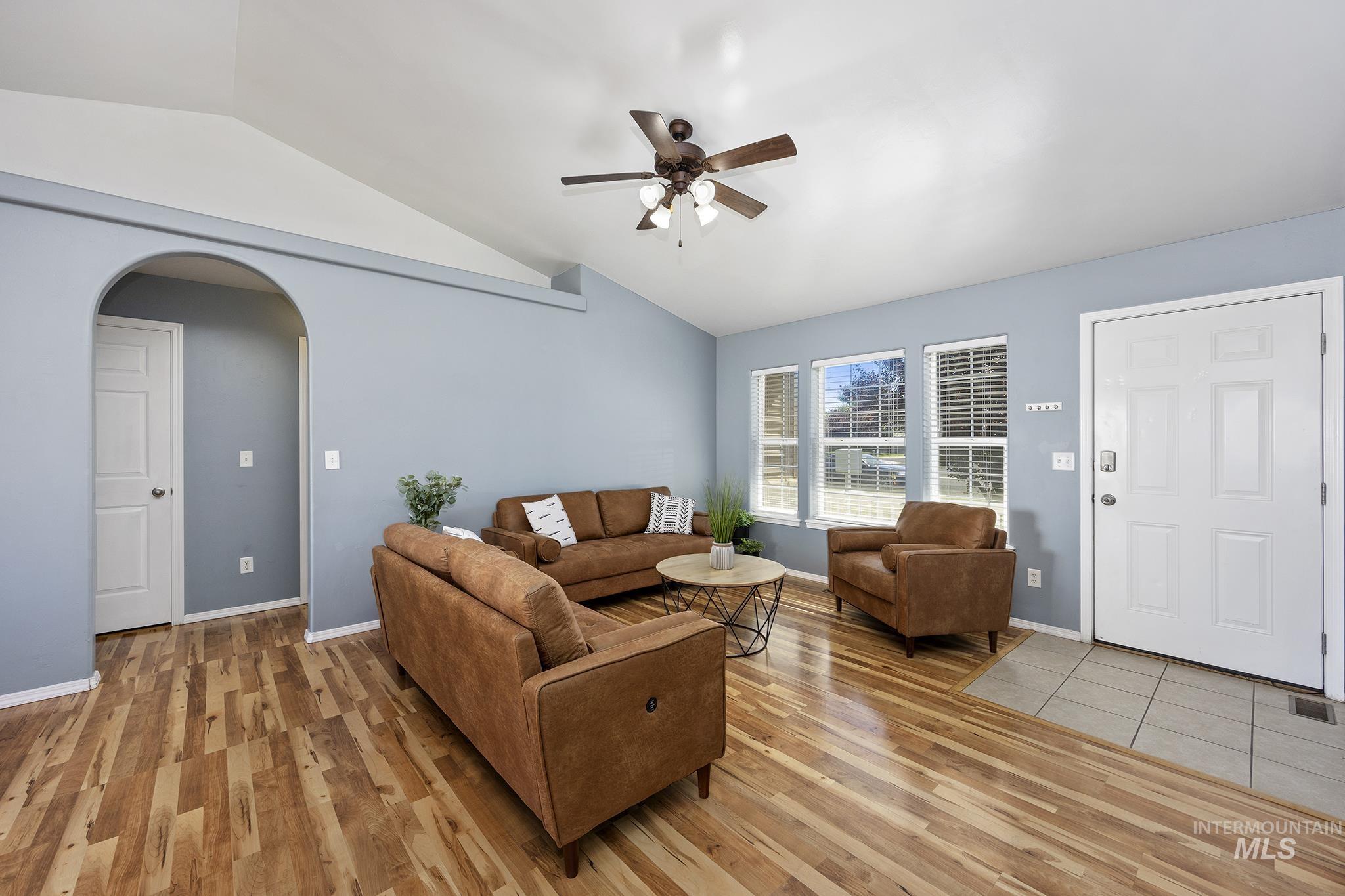 Living room with lofted ceiling, arched walkways, ceiling fan, and light wood finished floors