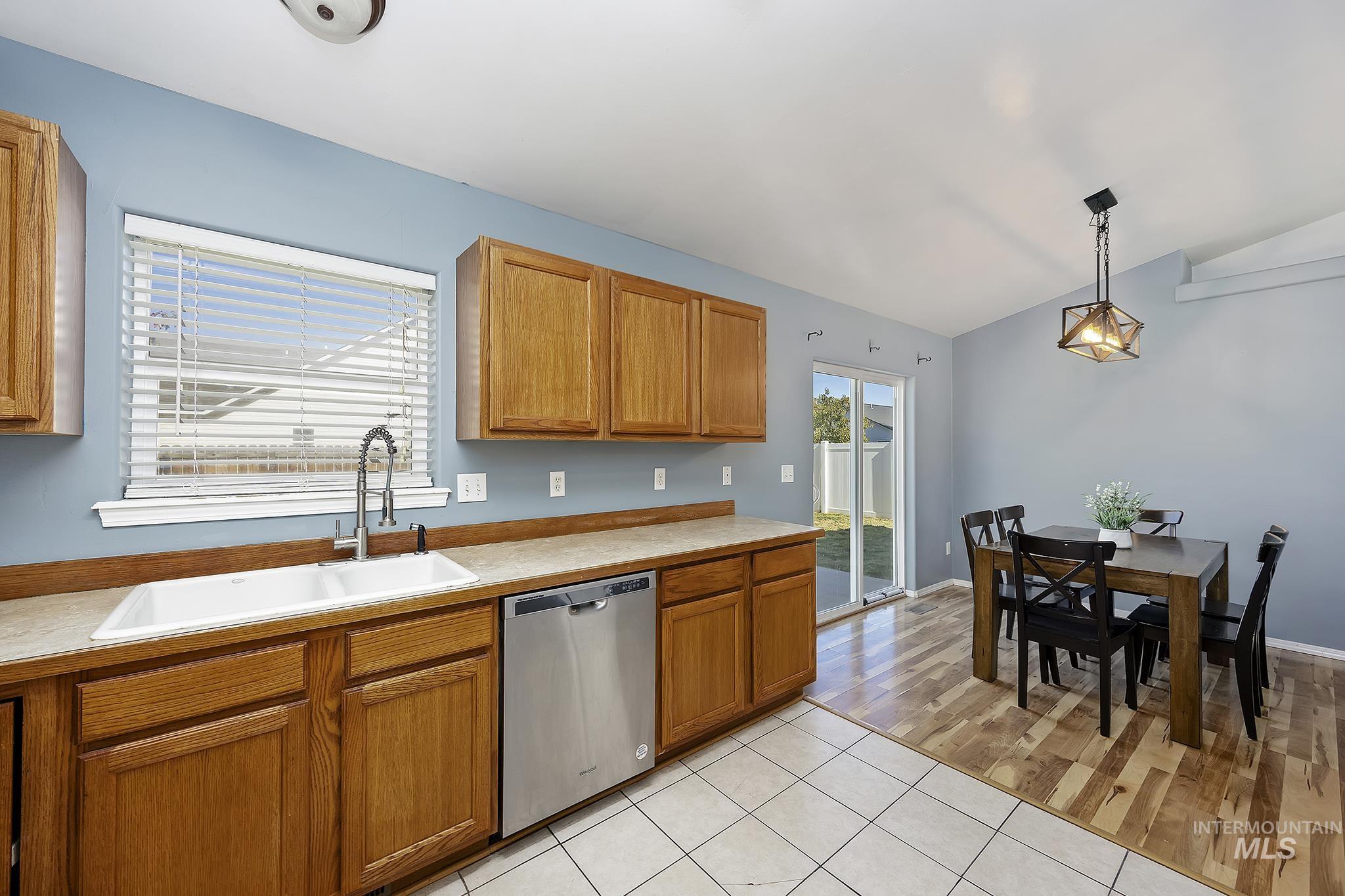 Kitchen with pendant lighting, light countertops, stainless steel dishwasher, light tile patterned floors, and lofted ceiling