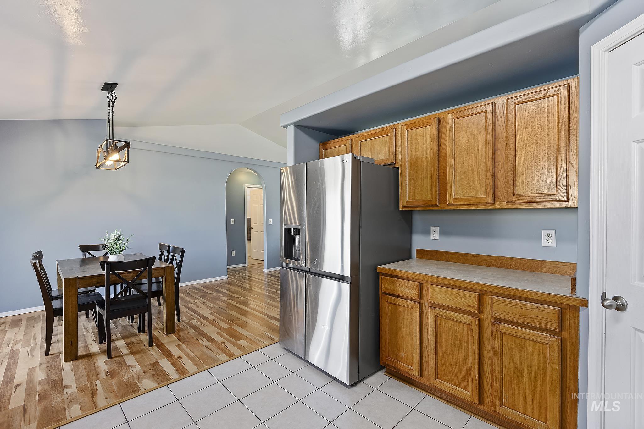 Kitchen featuring arched walkways, stainless steel refrigerator with ice dispenser, hanging light fixtures, light countertops, and vaulted ceiling