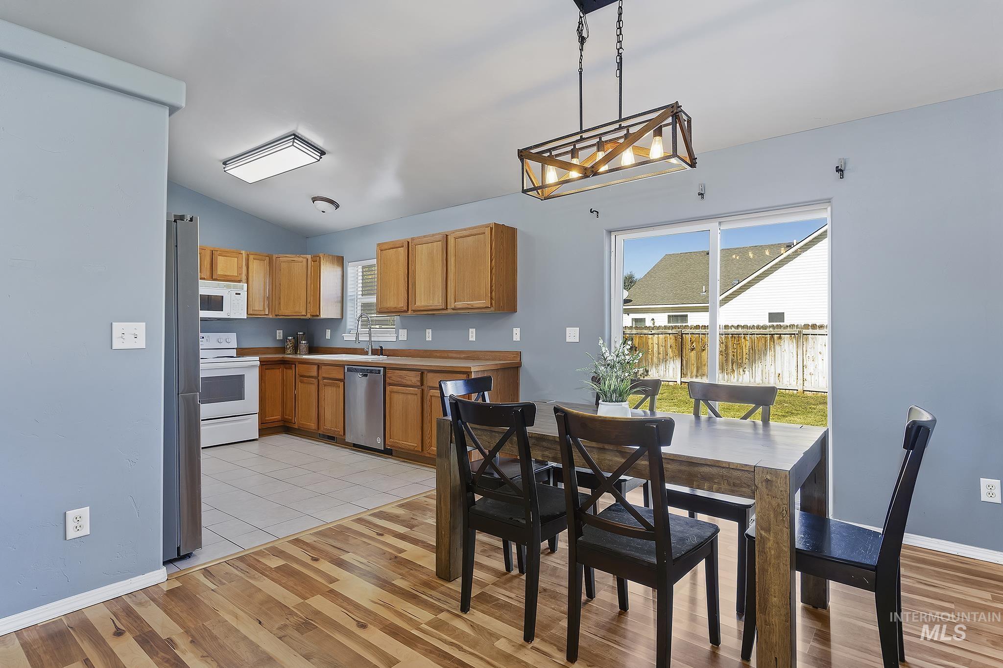 Kitchen featuring brown cabinets, stainless steel appliances, decorative light fixtures, vaulted ceiling, and plenty of natural light