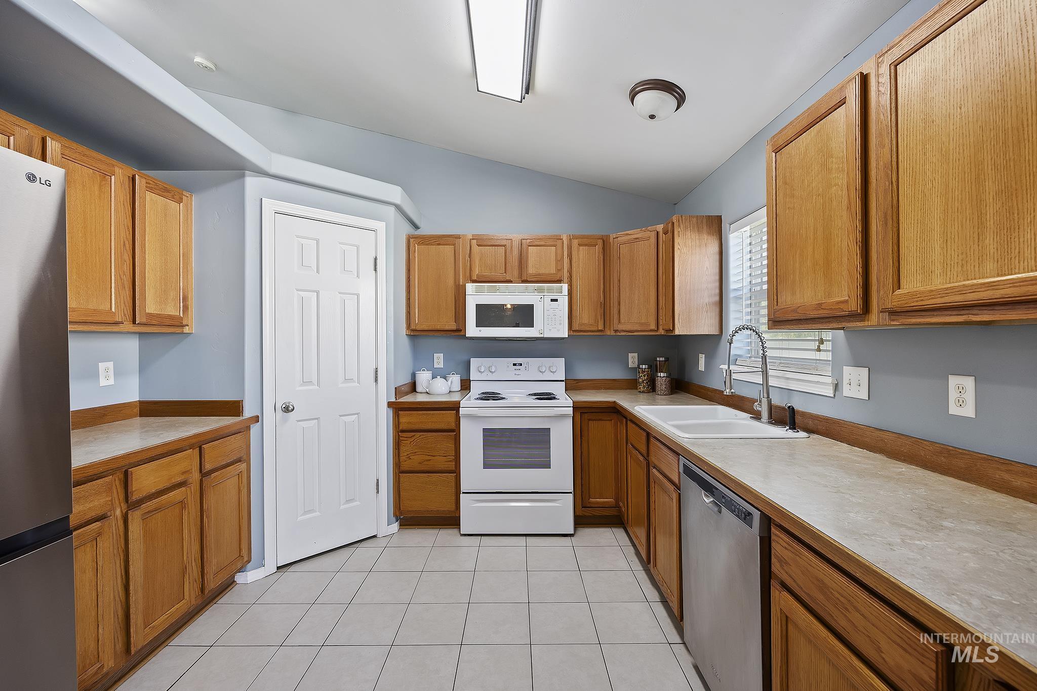 Kitchen with stainless steel appliances, light countertops, lofted ceiling, brown cabinets, and light tile patterned flooring
